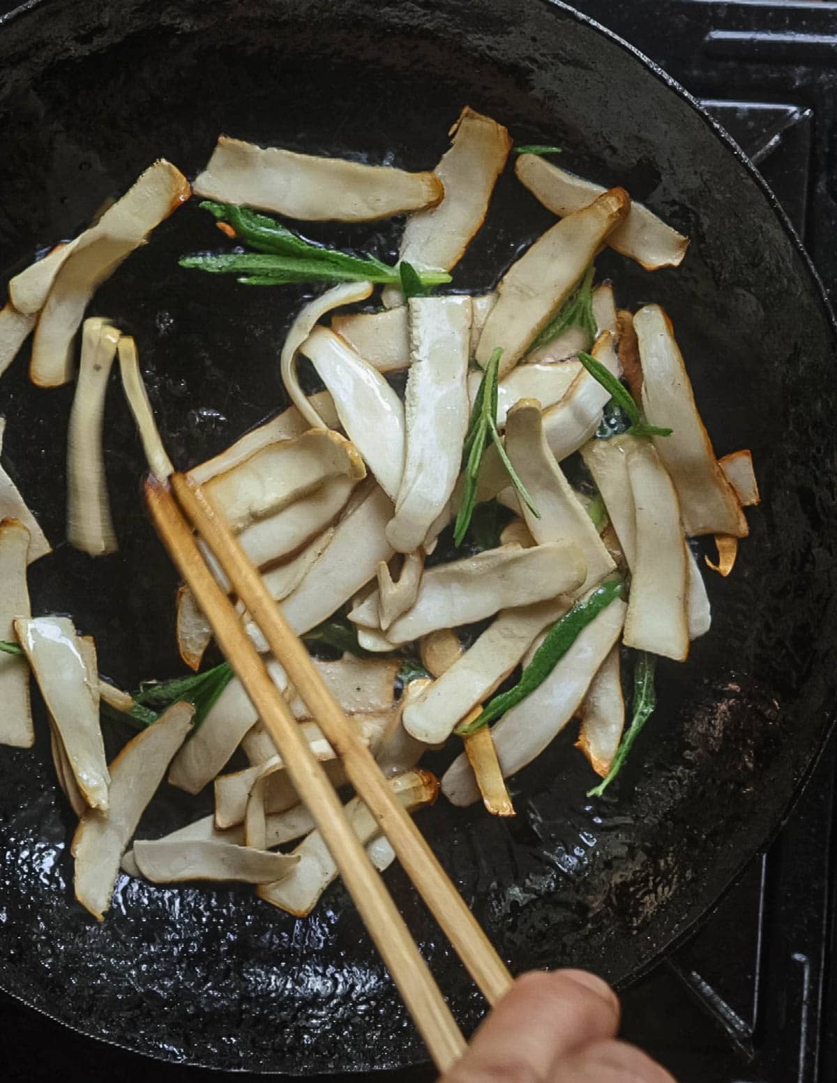 Adding fresh rosemary leaves to a pan of mushrooms cooking. 