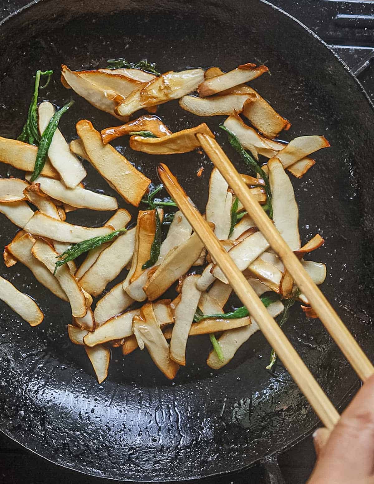 Stirring a pan of sliced polypore mushrooms in a pan with a wooden utensil. 