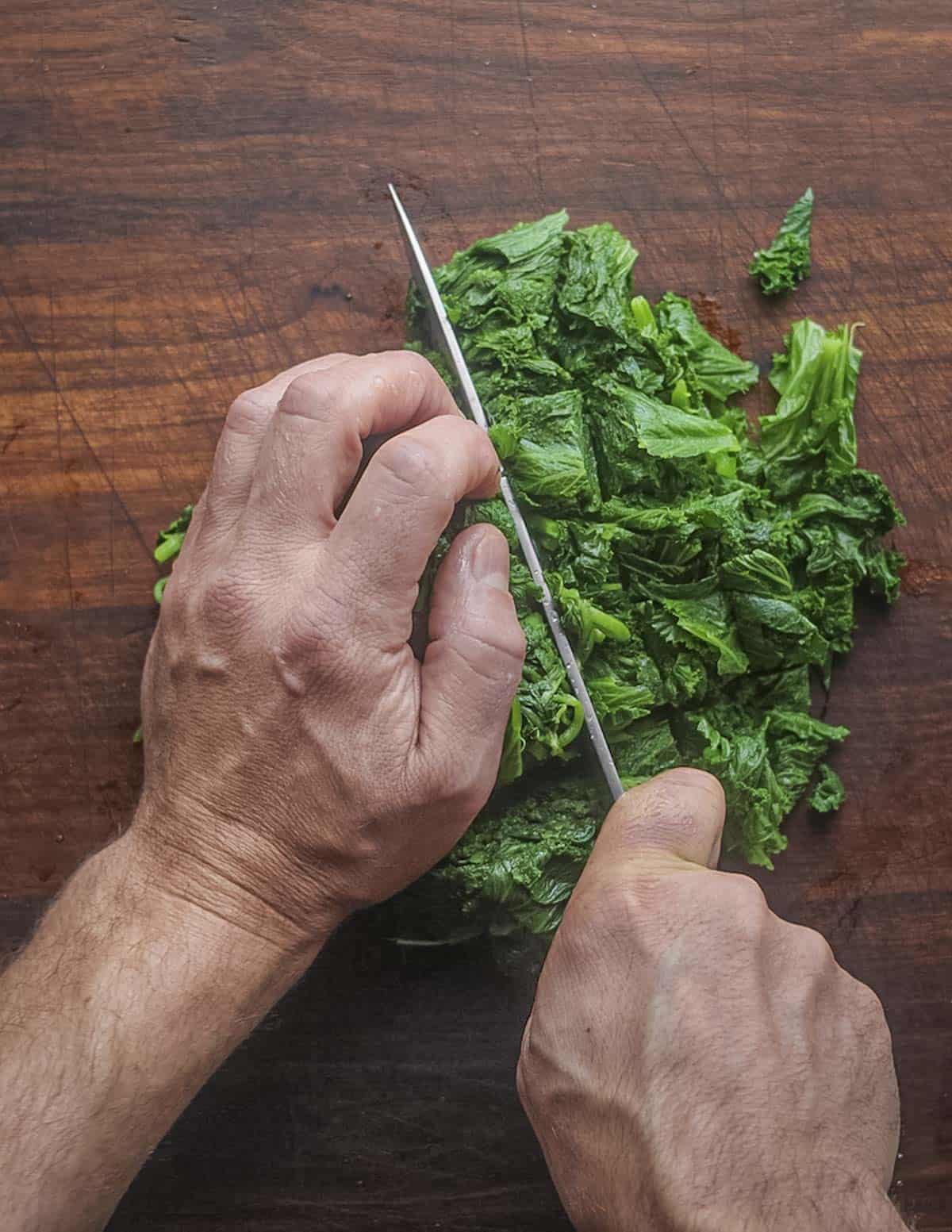 Chopping cooked greens to ensure they're an even texture. 