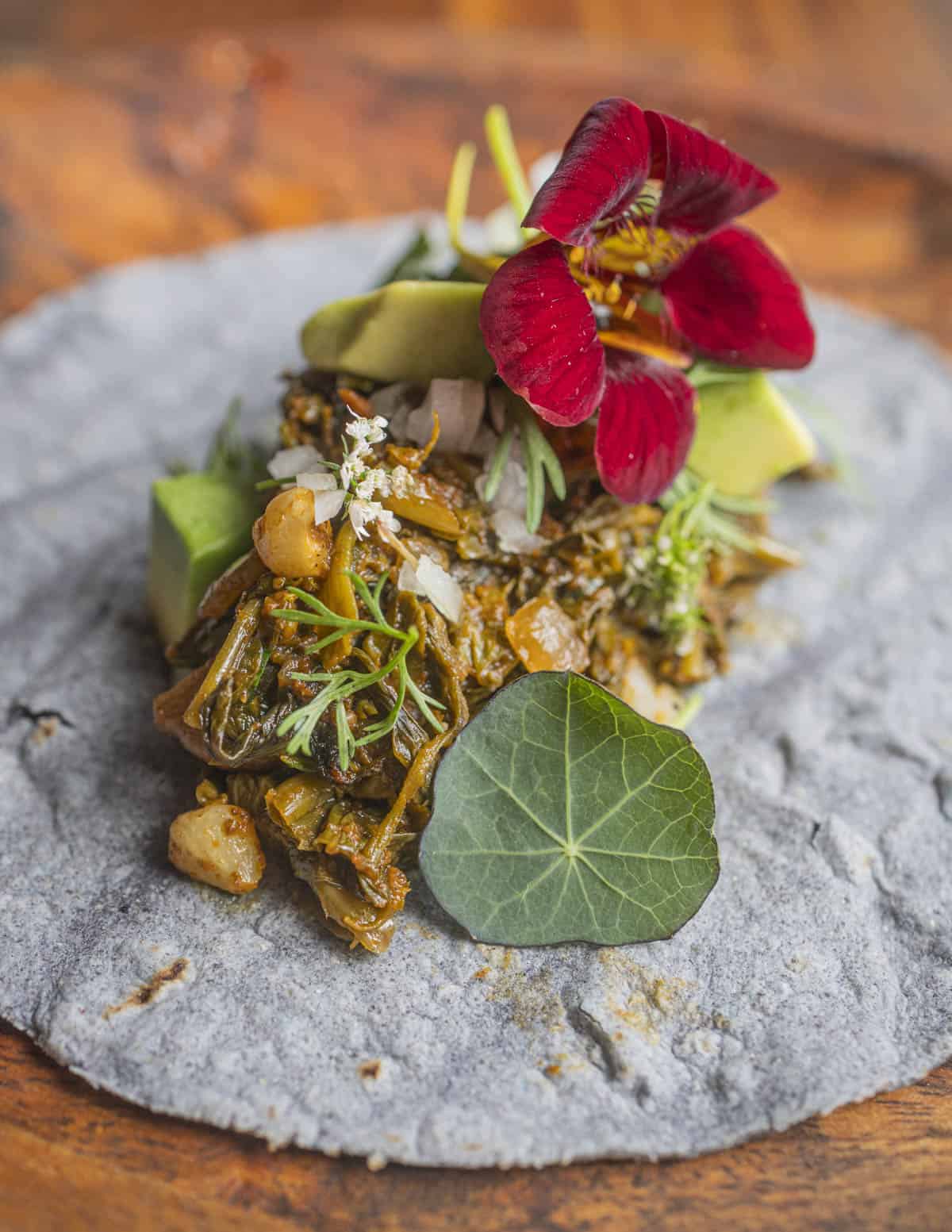 Plant based taco garnished with cilantro flowers, nasturtium flowers and leaves and avocado. 