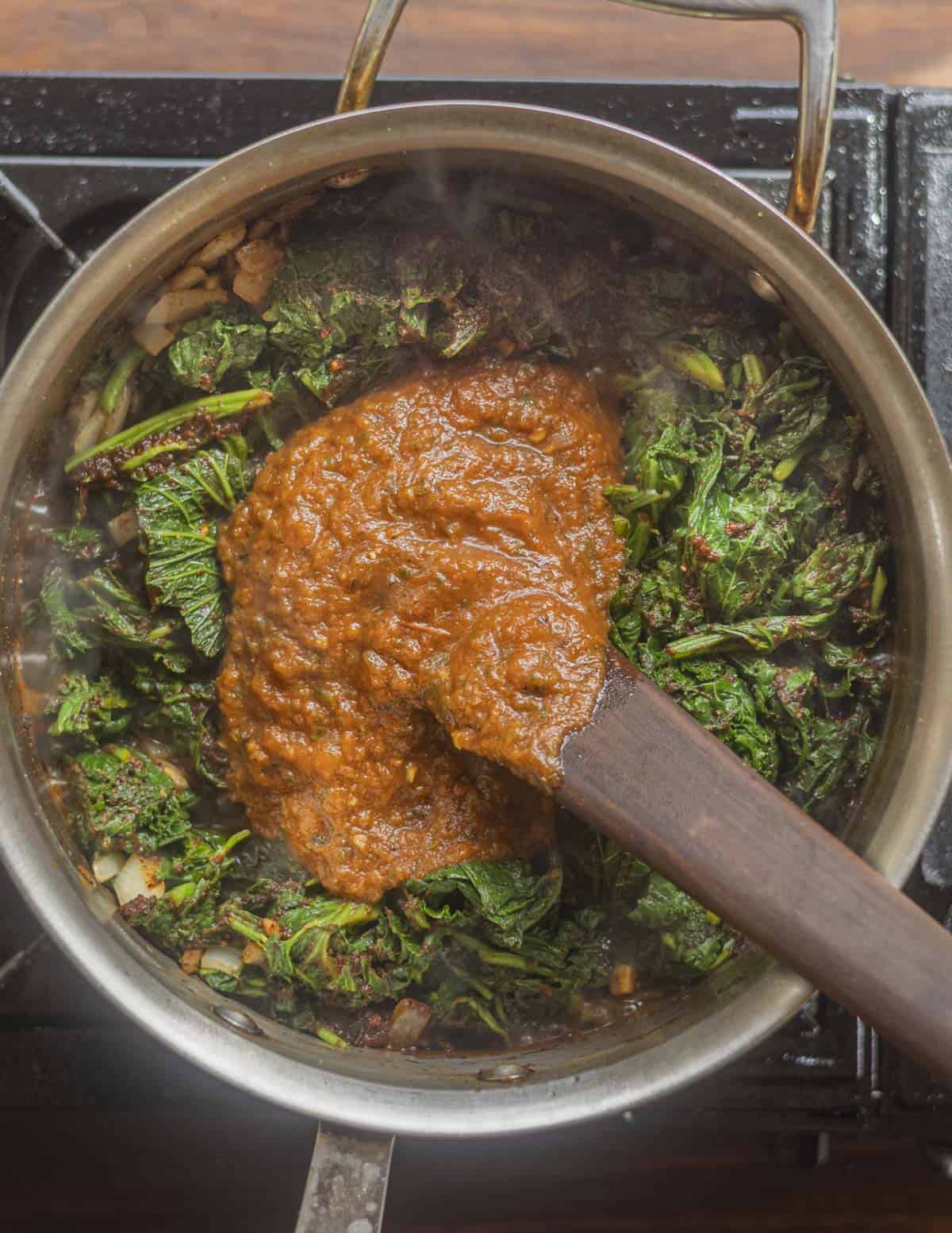 Adding greens and tomato-chili sauce to a pot. 