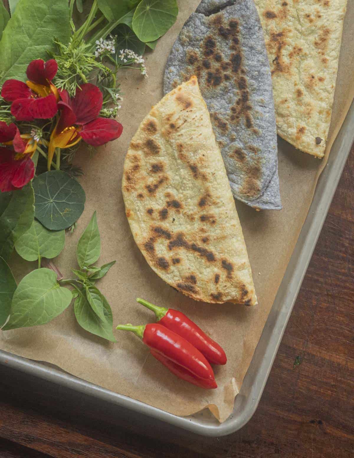 Plant based quesadillas surrounded by fresh greens and peppers, herbs and nasturtium flowers. 