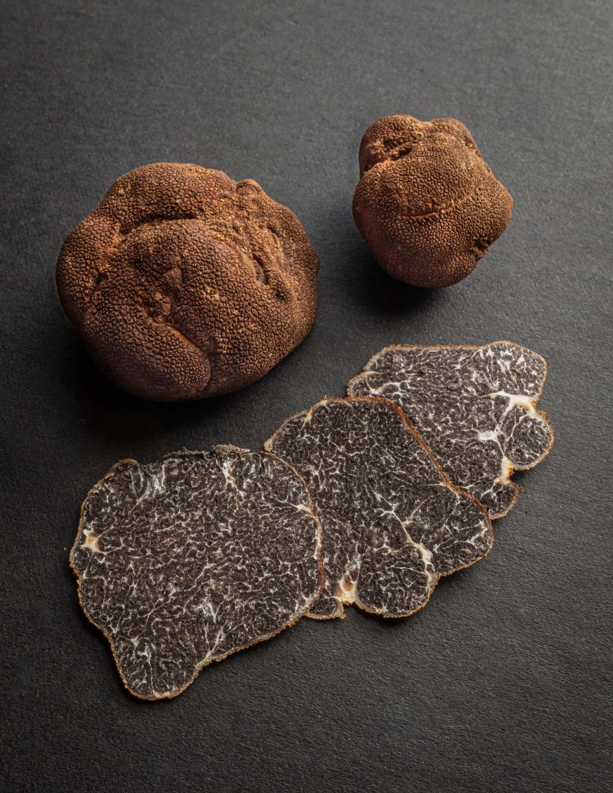 Appalachian truffles or Tuber canaliculatum on a black background with one truffle sliced in the foreground showing the inner marbled surface.