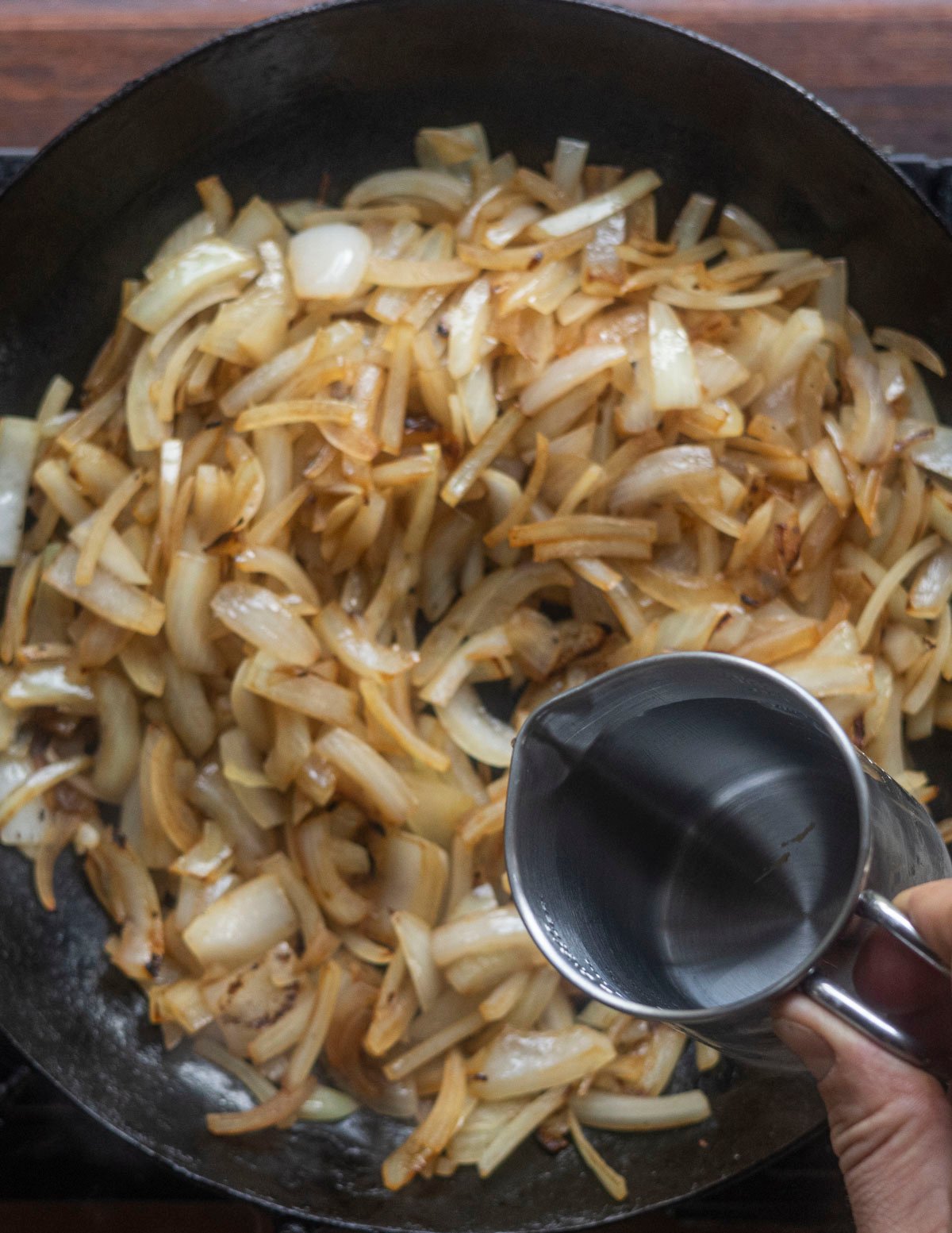 Adding a splash of water to onions to deglaze the pan. 