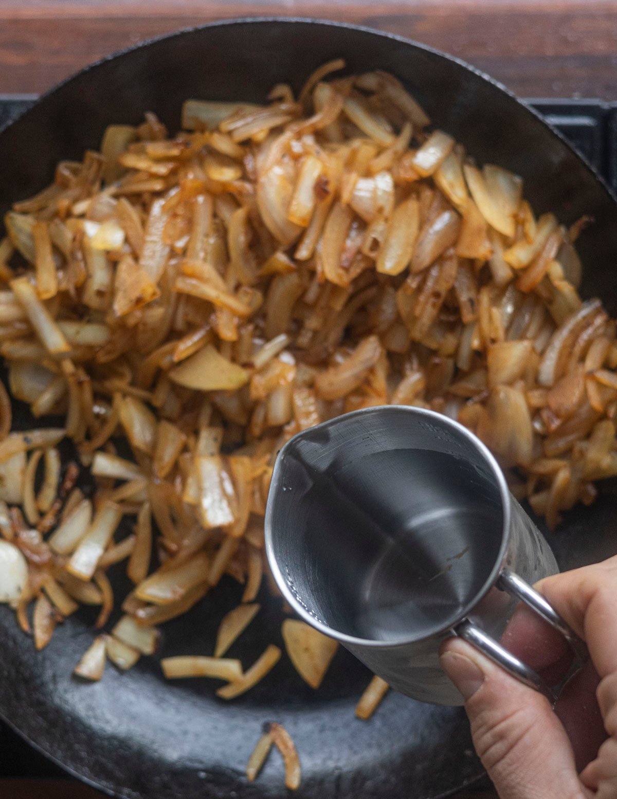 Adding more water to a pan of caramelizing onions to continue browning them. 