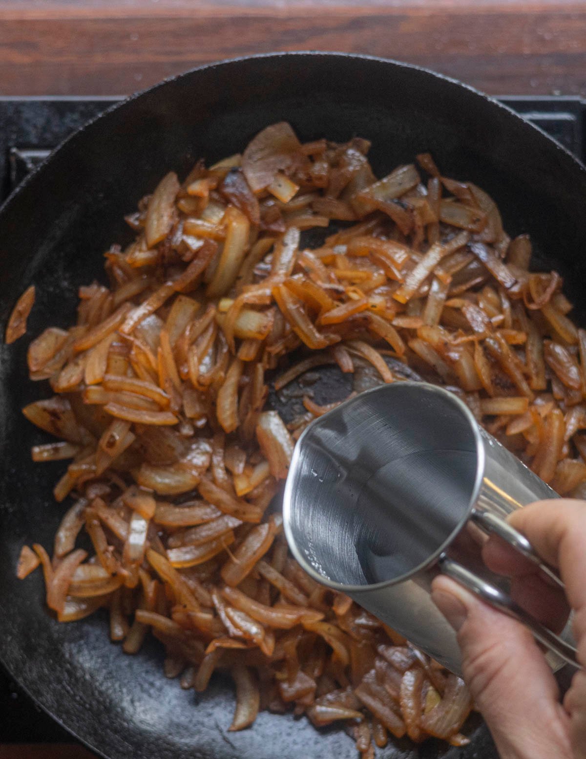 Adding more water to a pan of caramelized onions to deglaze the pan. 