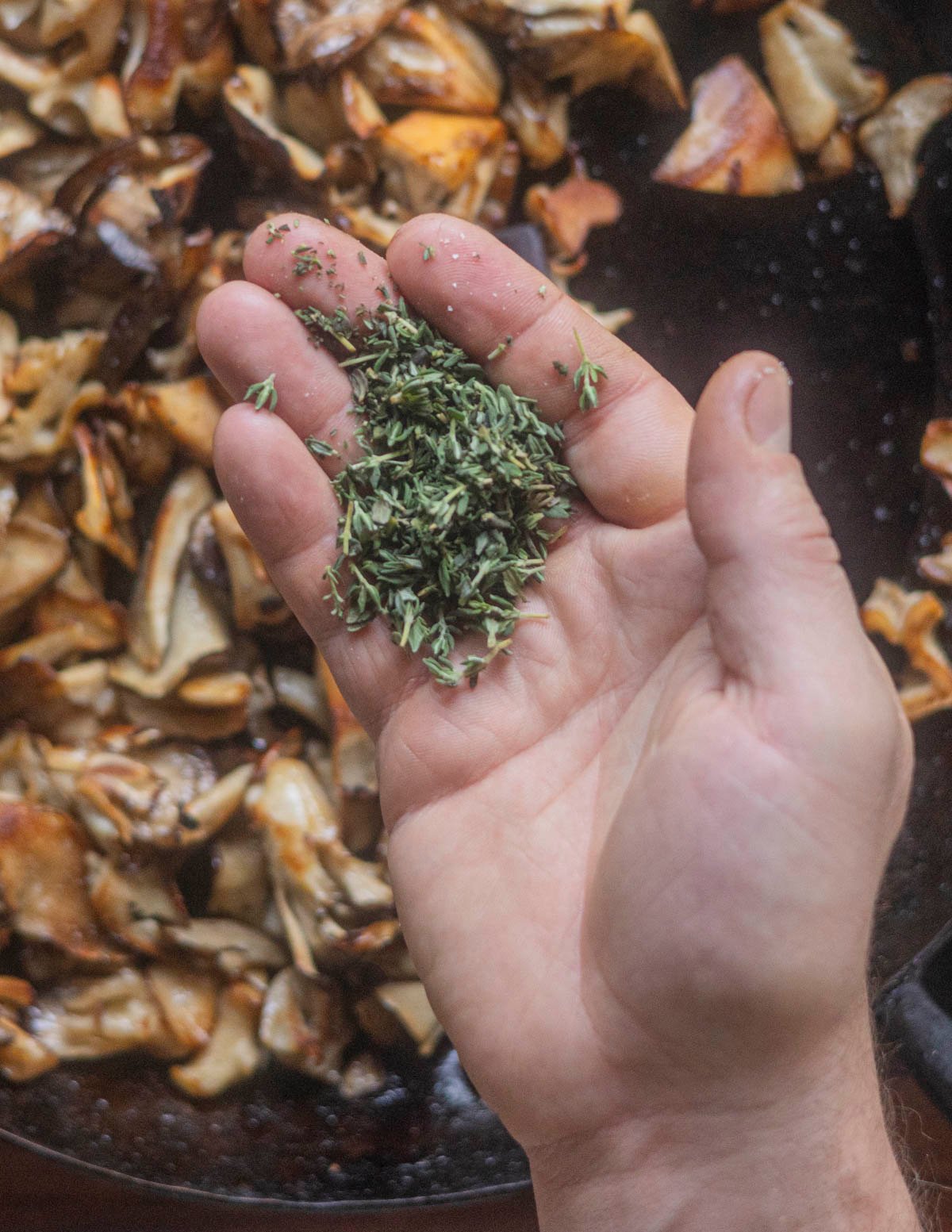 Adding fresh thyme to a pan of cooking mushrooms. 