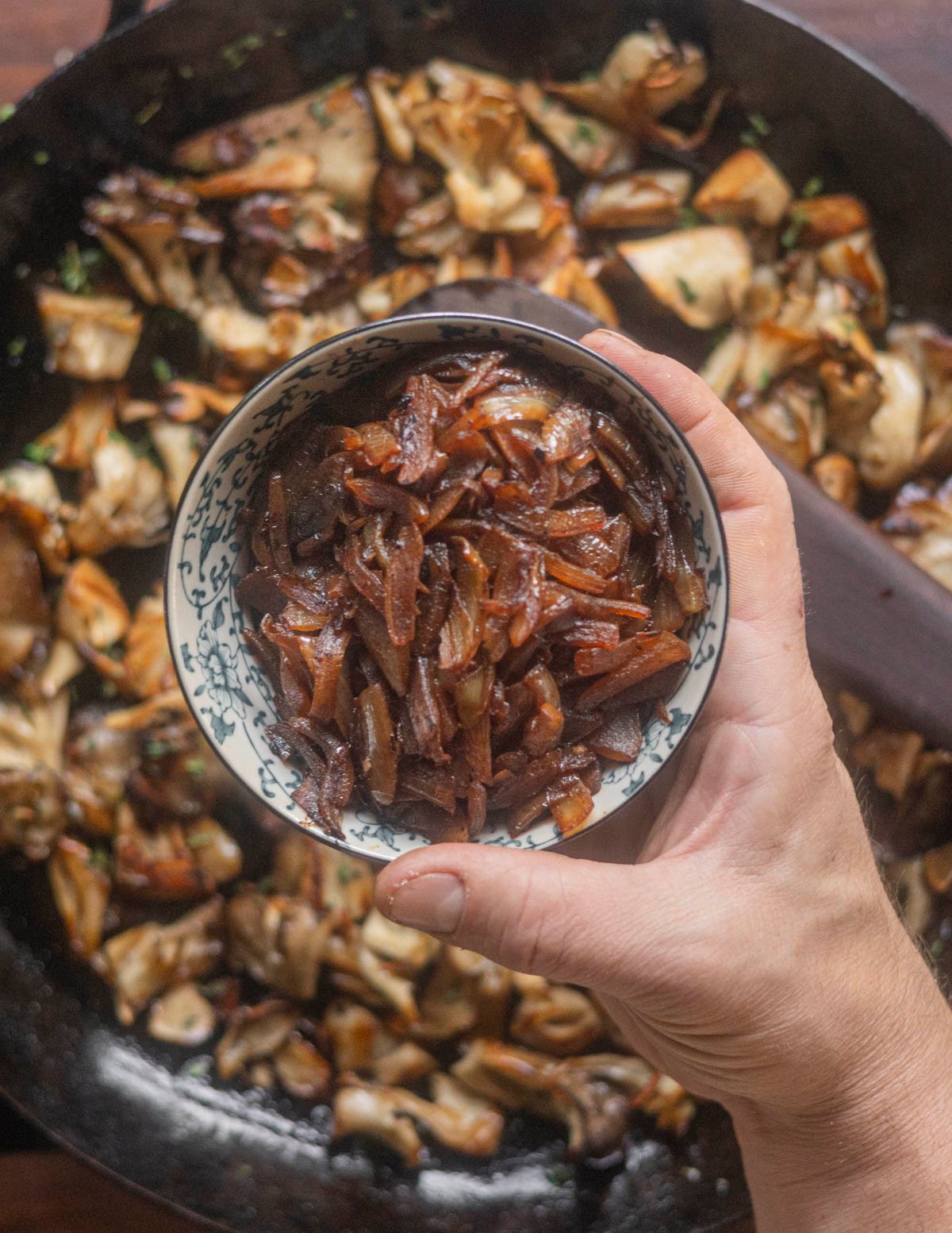 Adding the caramelized onions to a pan of cooked mushrooms. 