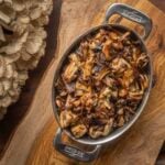 A dish of caramelized onions and mushrooms next to a large mushroom on a cutting board.