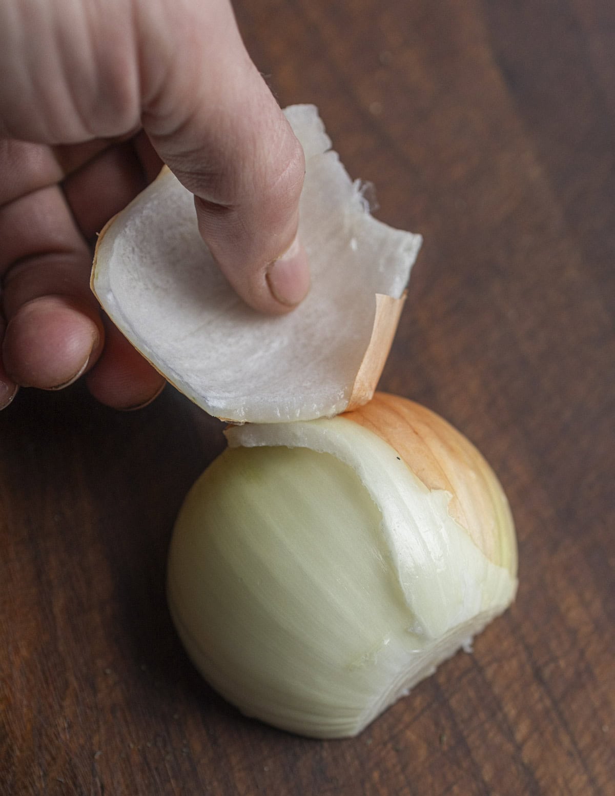 Removing the inner layer of skin from an onion before slicing.