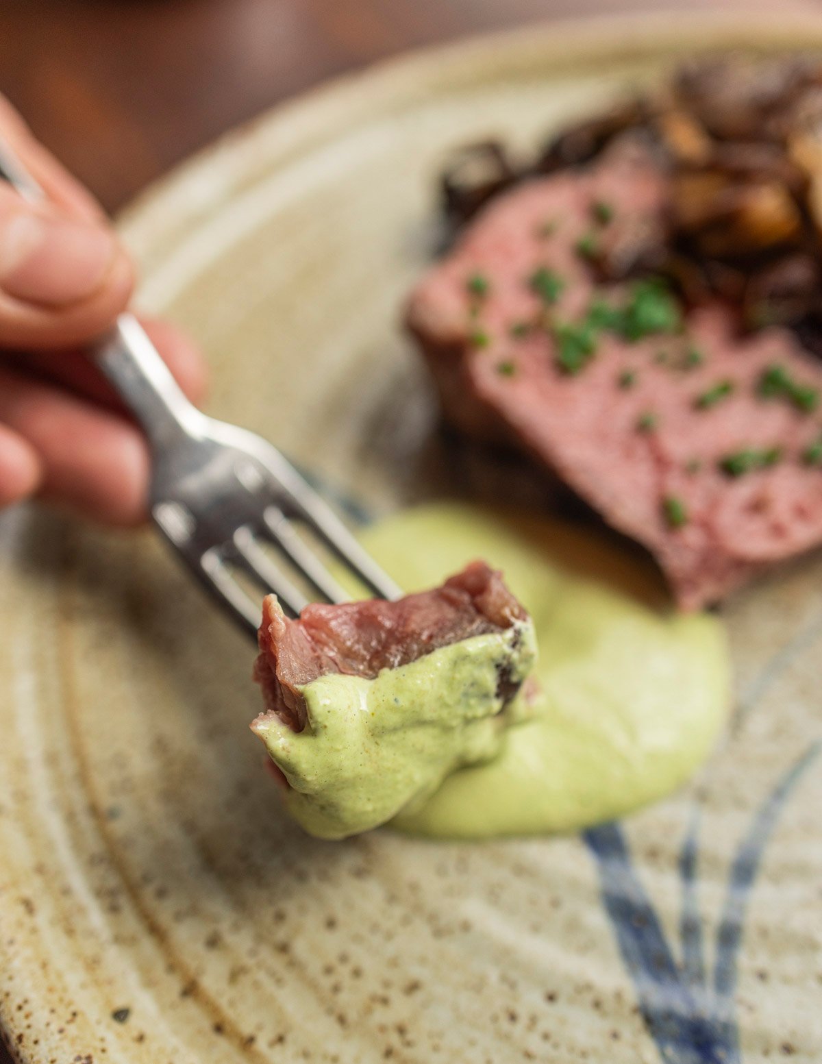 A perfectly cooked steak being dipped into a green aioli sauce. 