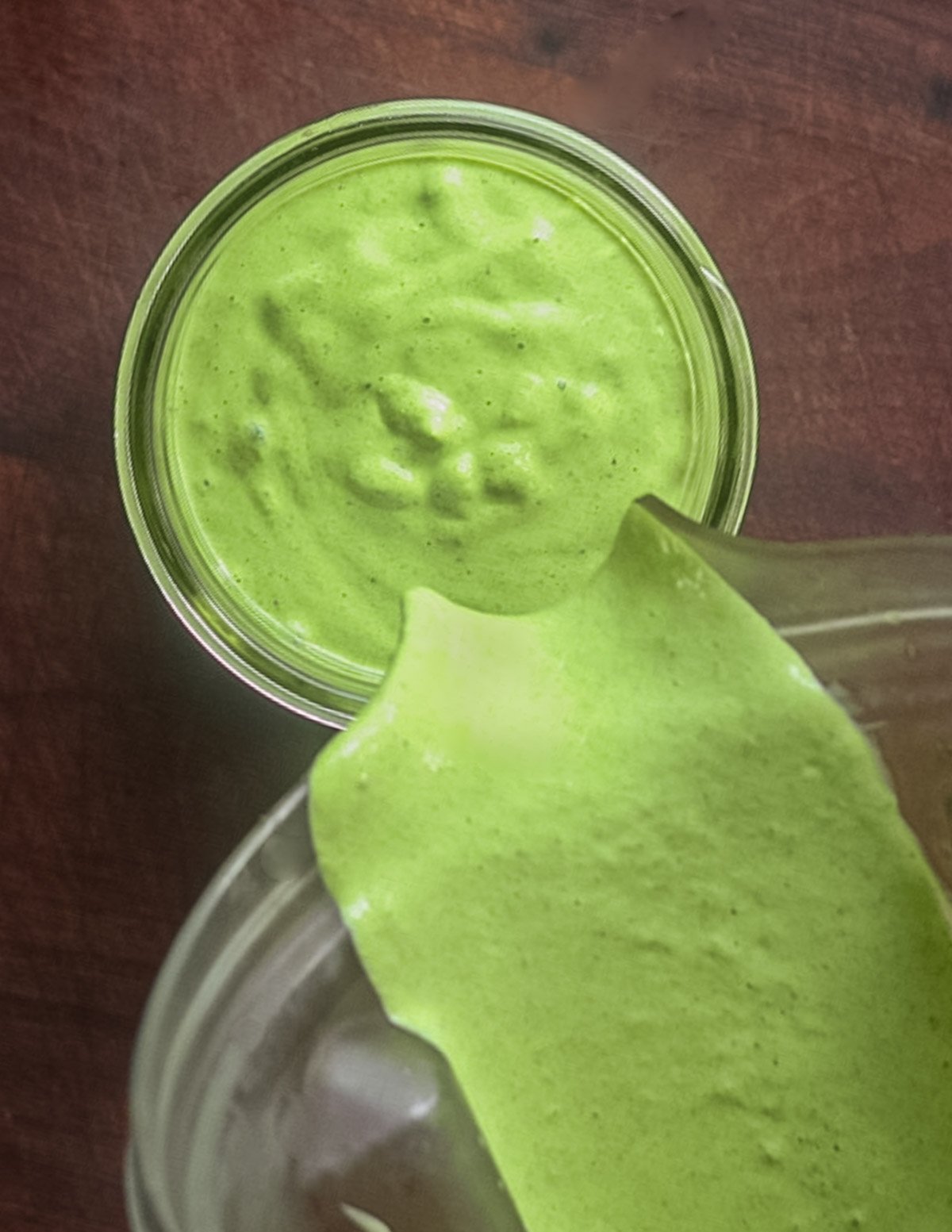 Pouring a bright green garlic herb aioli into a mason jar from a blender. 