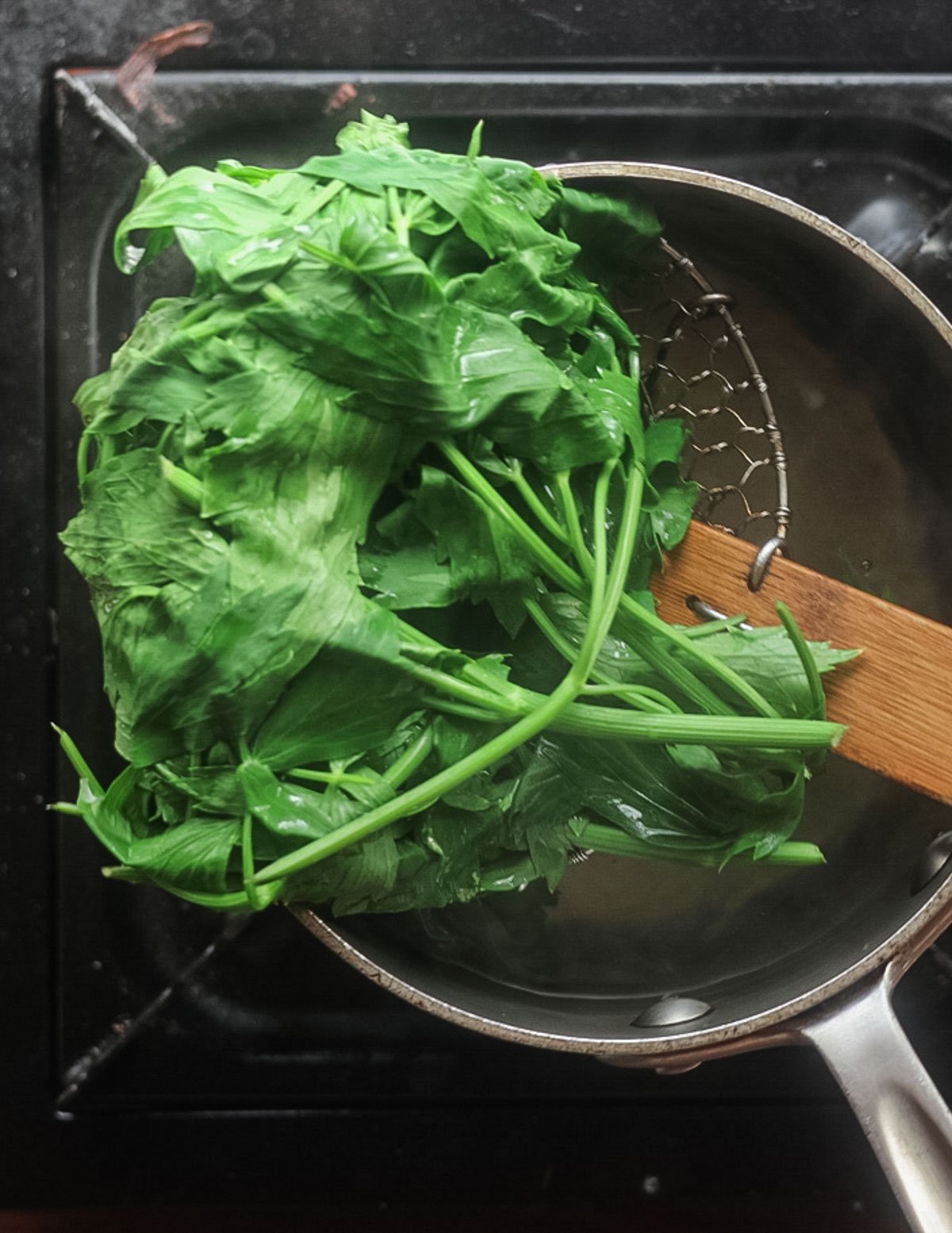 Removing blanched lovage greens from a pot of boiling water. 