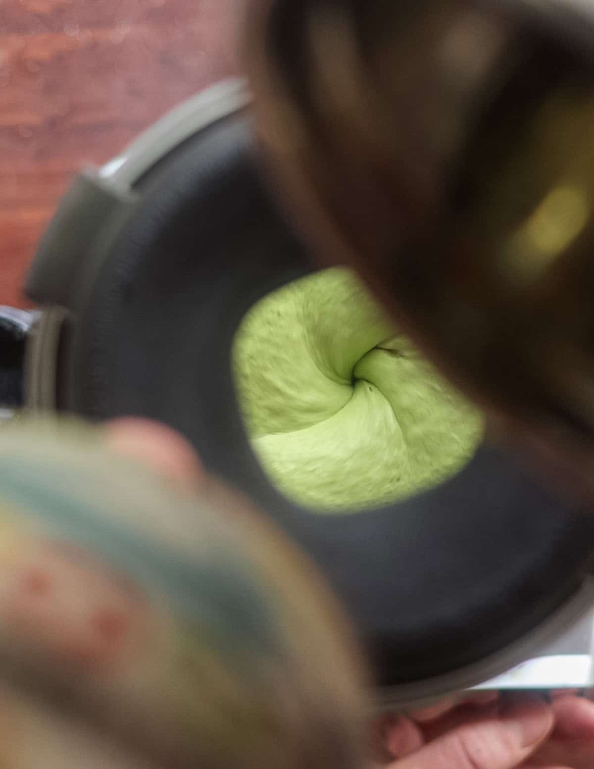 A man watching carefully while slowly pouring oil into a blender to make green garlic herb aioli with lovage. 