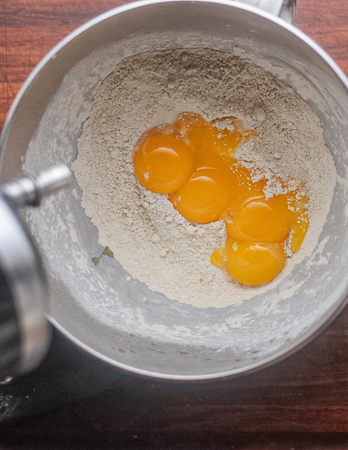 Adding egg yolks to mixed chestnut flour and all purpose flour in a stand mixer. 