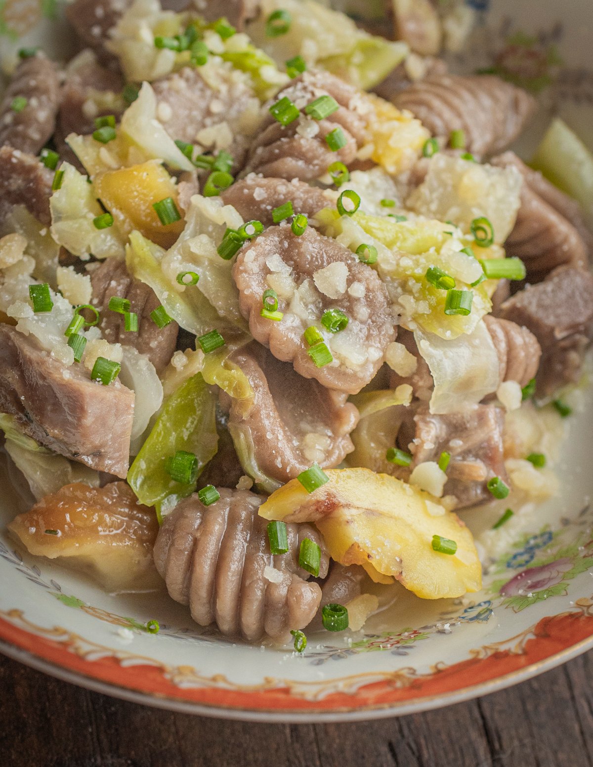 A close up image of a pan of chestnut flour gnocchi with goose confit, cabbage and roasted chestnuts.