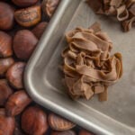 Homemade chestnut flour pasta on a baking tray surrounded by fresh chestnuts.