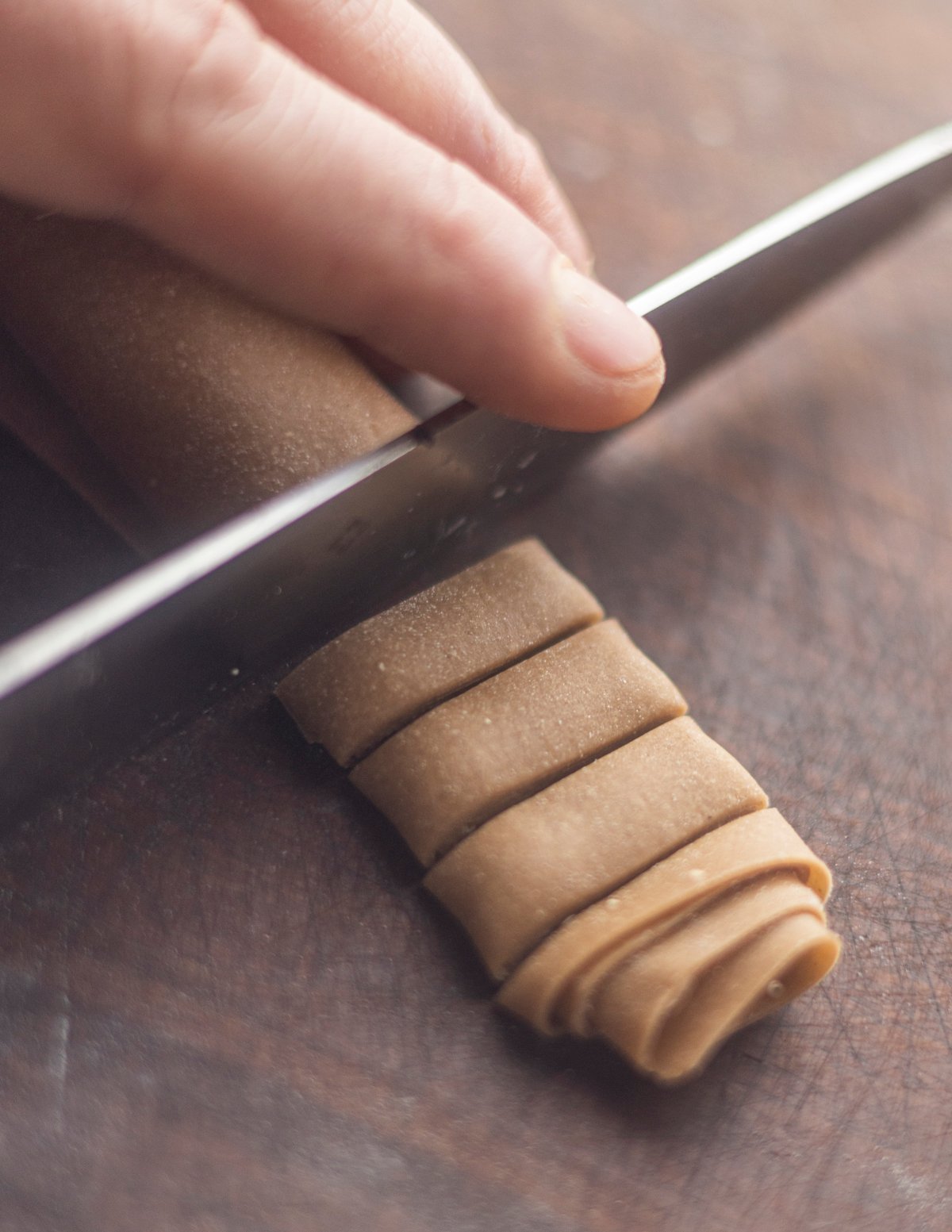 Cutting a sheet of rolled chestnut pasta dough into noodles with a knife. 