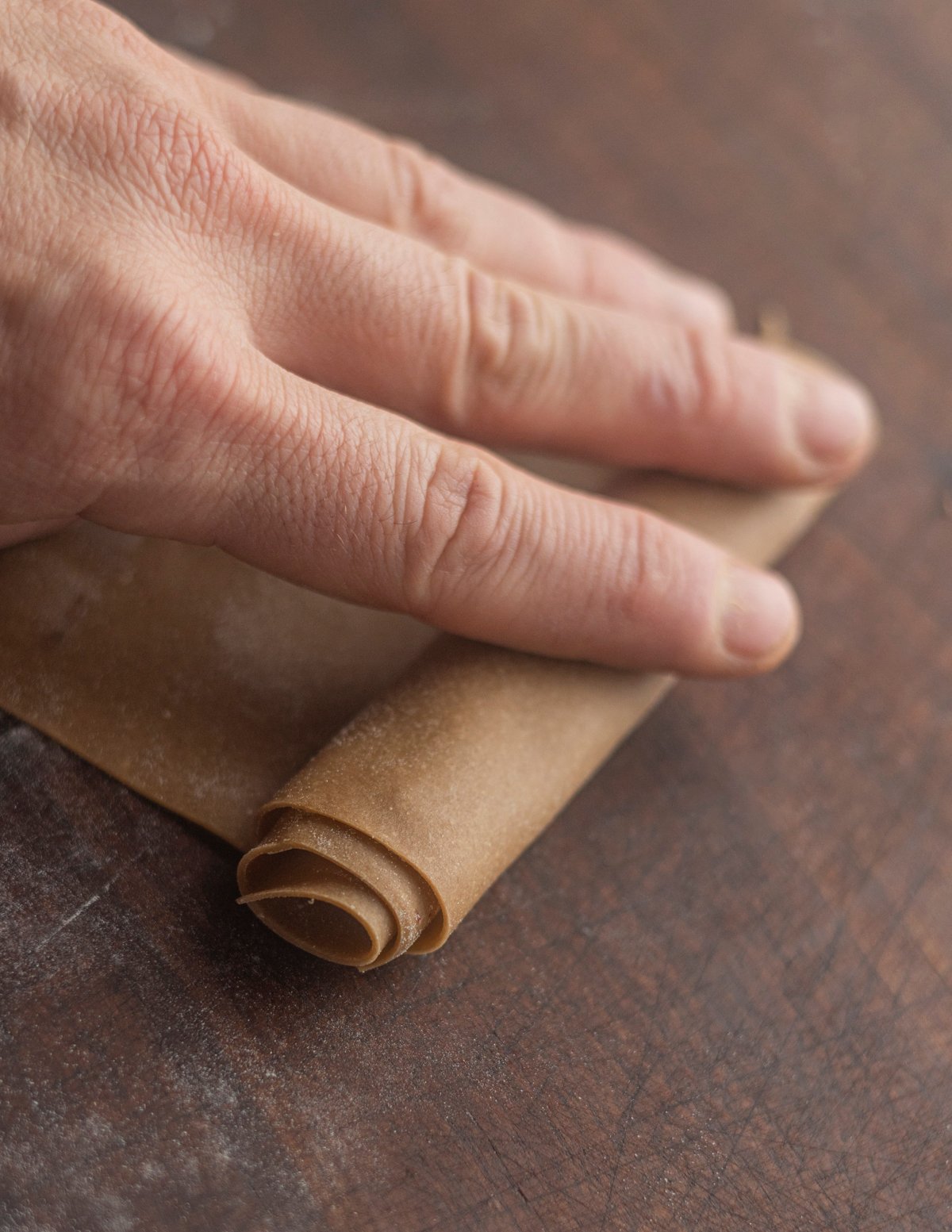 Rolling a sheet of pasta dough before slicing into noodles. 