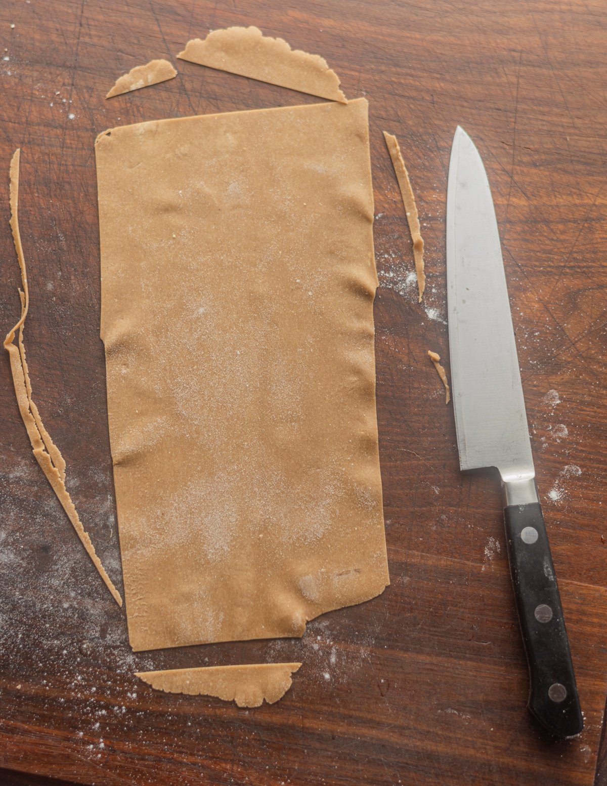 Trimming rough edges from brown pasta dough made from chestnut flour. 