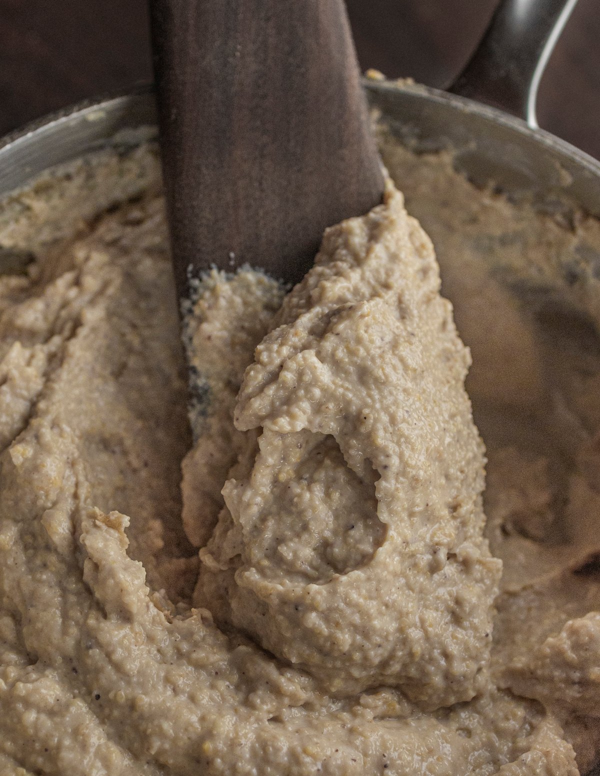 A spatula stirring a pot of chestnut polenta made with homemade flour showing a coarse texture. 