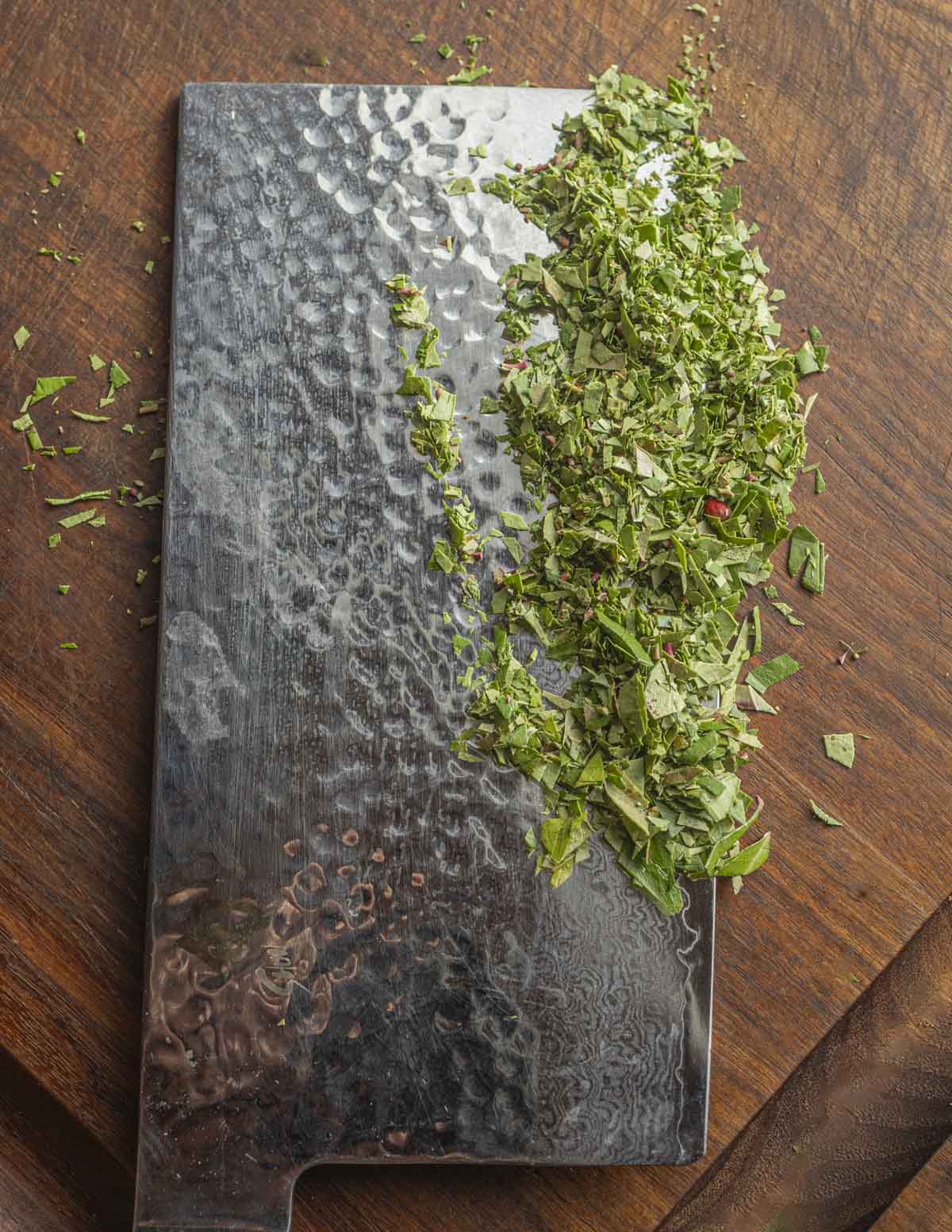 A large chef knife showing finely minced teaberry or wintergreen leaves. 