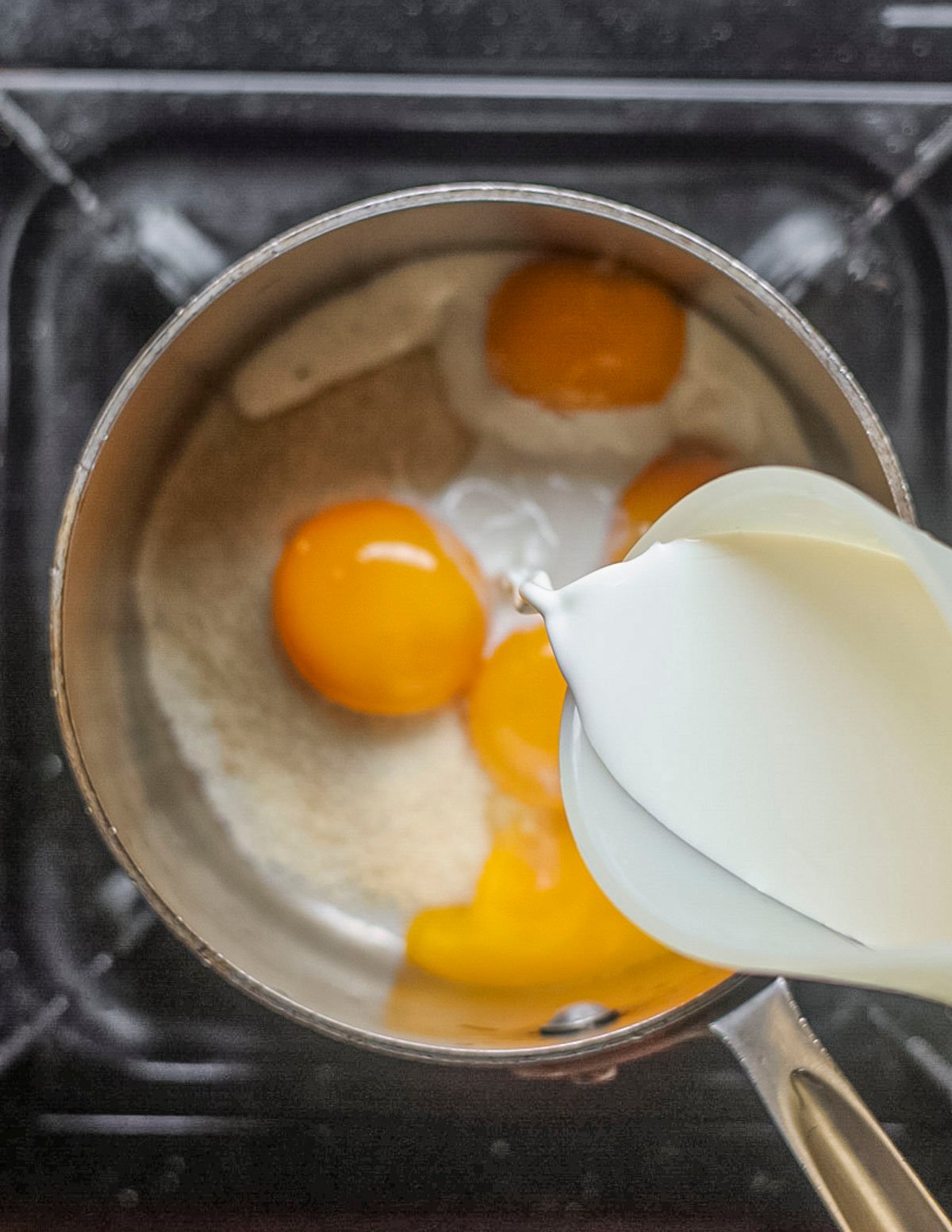 Adding cream and milk to a pan of egg yolks and sugar to make ice cream. 