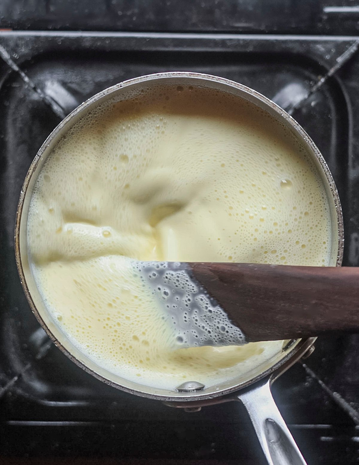 Stirring an ice cream custard base as it cooks with a wooden spatula. 