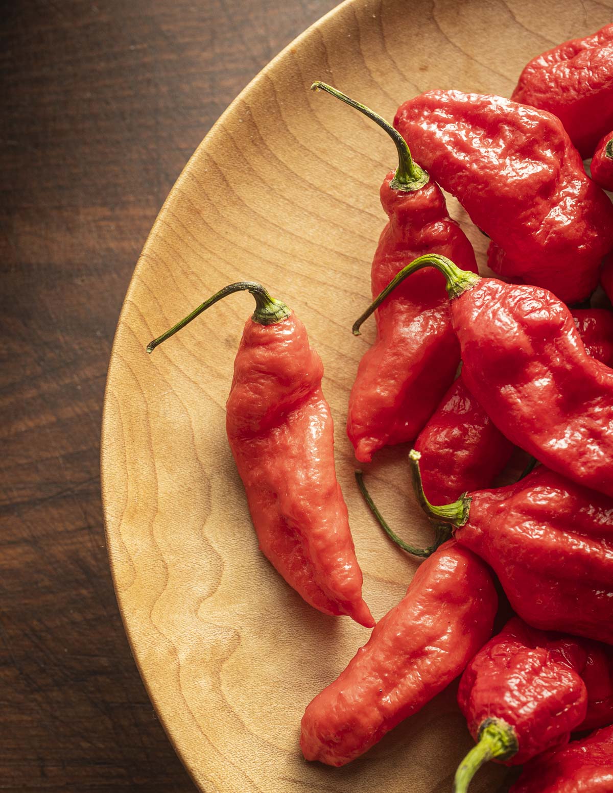 Fresh red ghost peppers on a wooden plate. 