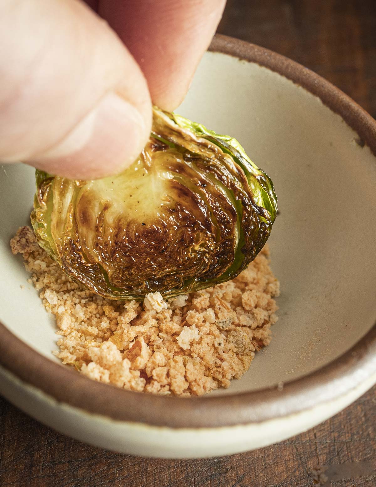 A hand dipping a Brussels sprout into a small bowl of hot pepper salt. 