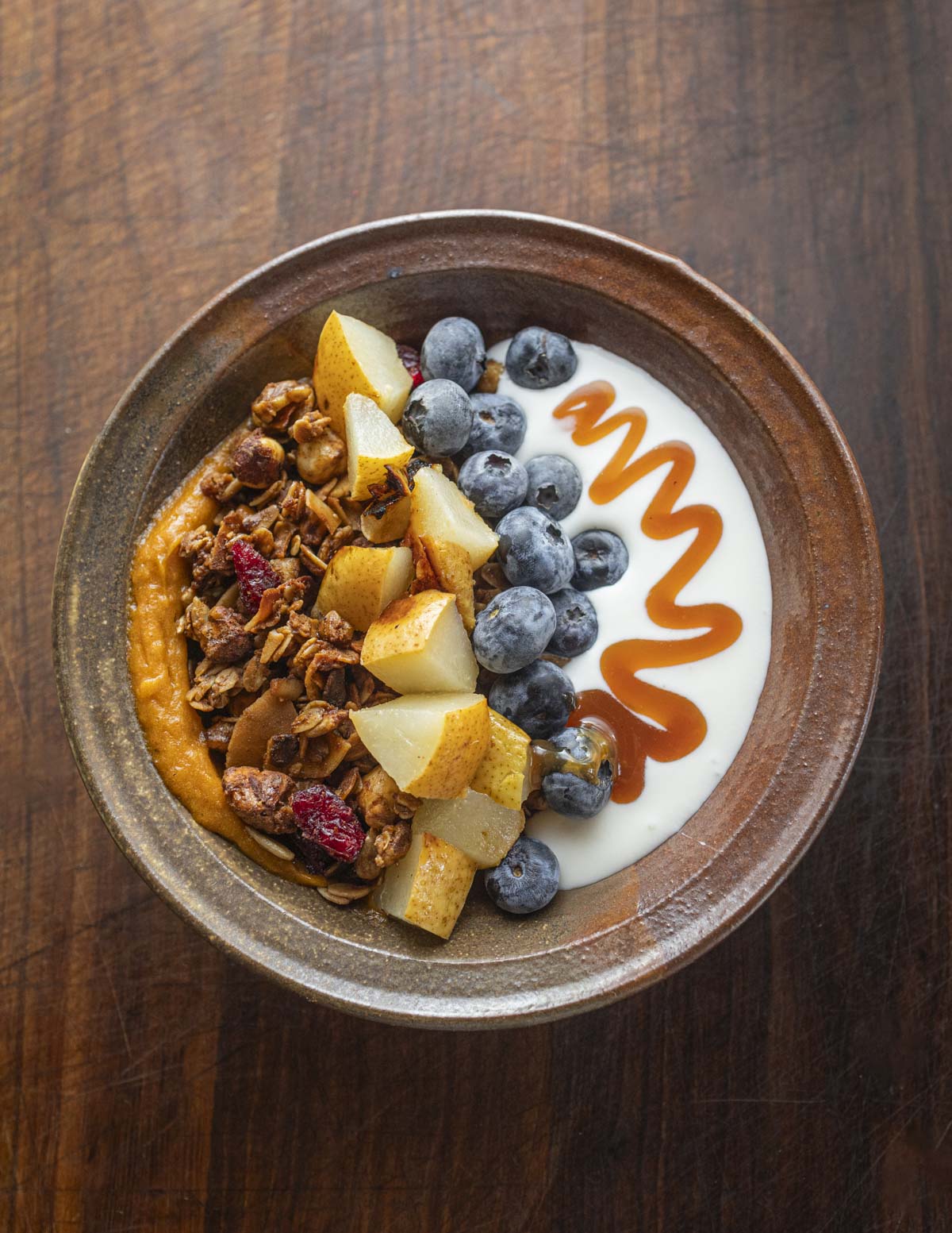 A bowl of granola and homemade yogurt with wild persimmon puree, black walnuts, blueberries, roasted pears and pear syrup.