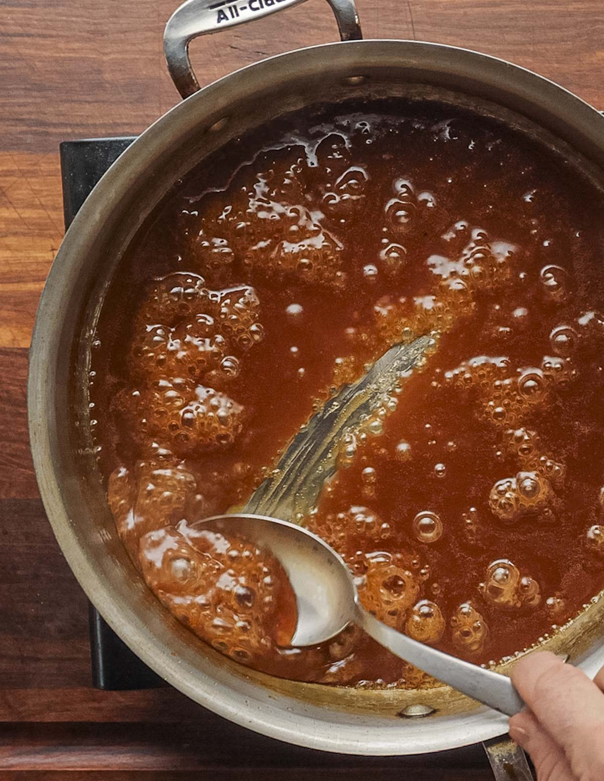 Dragging a spoon through a pan of pear caramel syrup showing the bottom of the pan can be seen. 