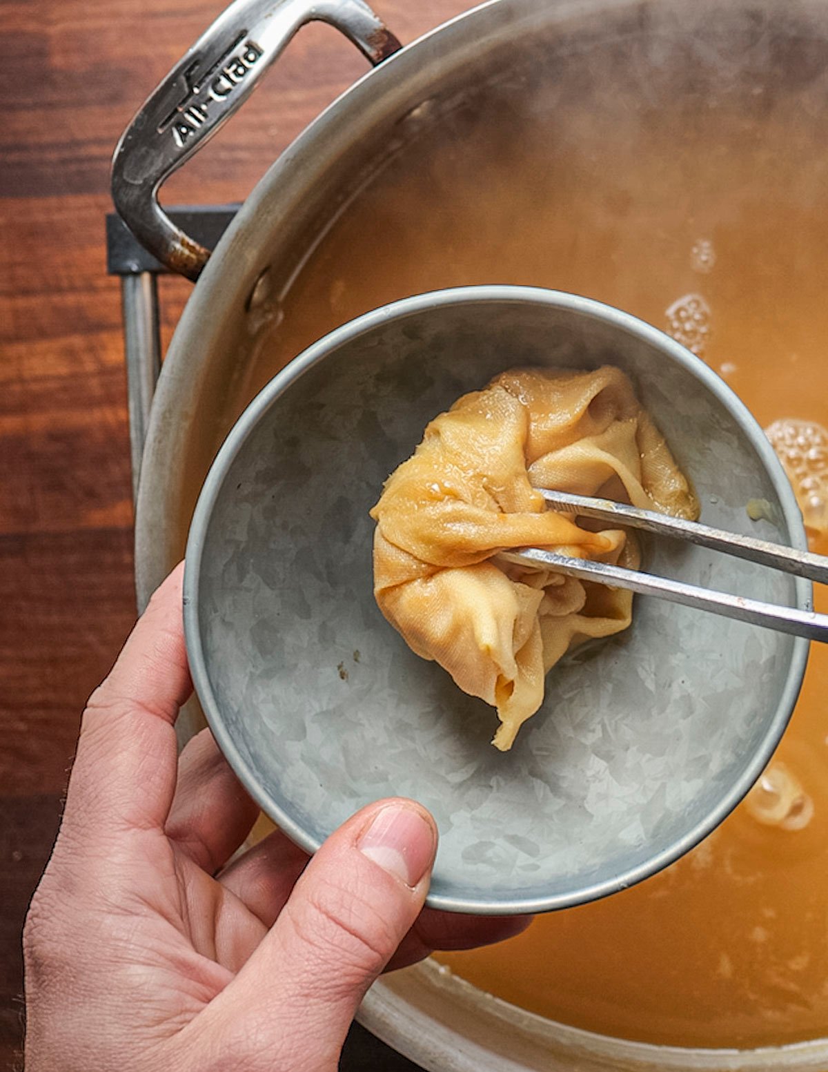 Removing a spice bouquet from a pan of pear juice cooking. 