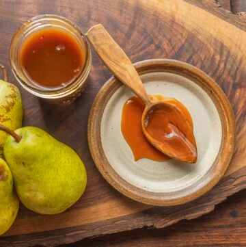 A wooden spoon filled with pear caramel syrup next to fresh pears and a jar of pear syrup.