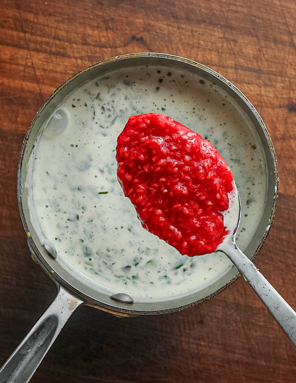 Adding a spoonful of crushed raspberries to an ice cream custard base. 