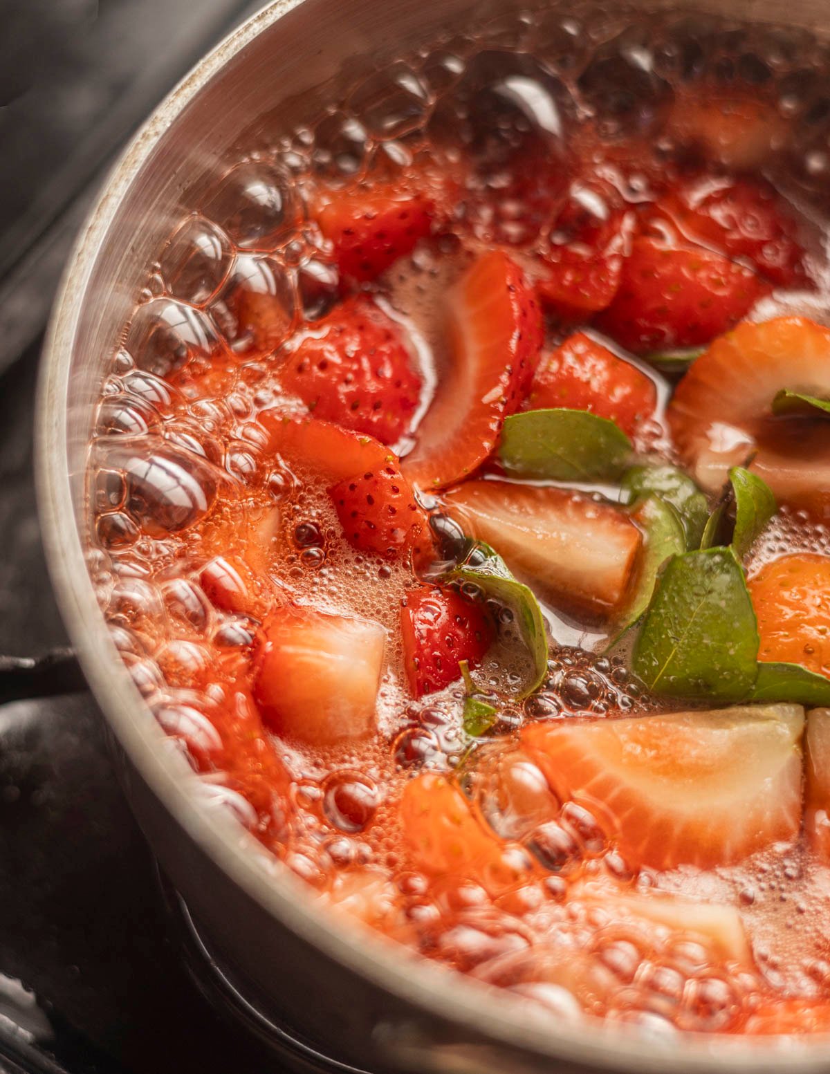 Strawberries cooking in a pan with wintergreen leaves. 