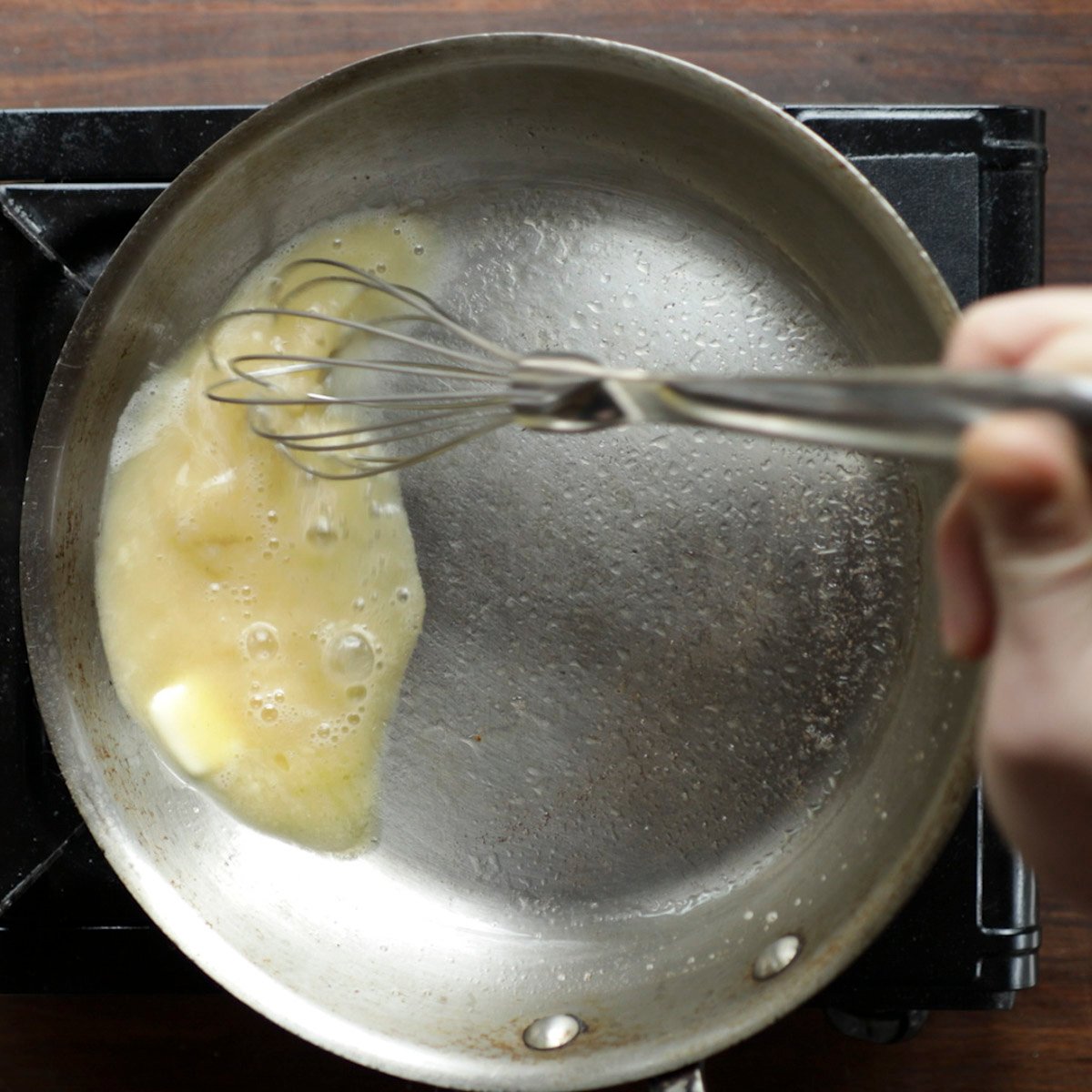 Whisking a pan of white wine brown butter sauce to emulsify it with cold butter. 