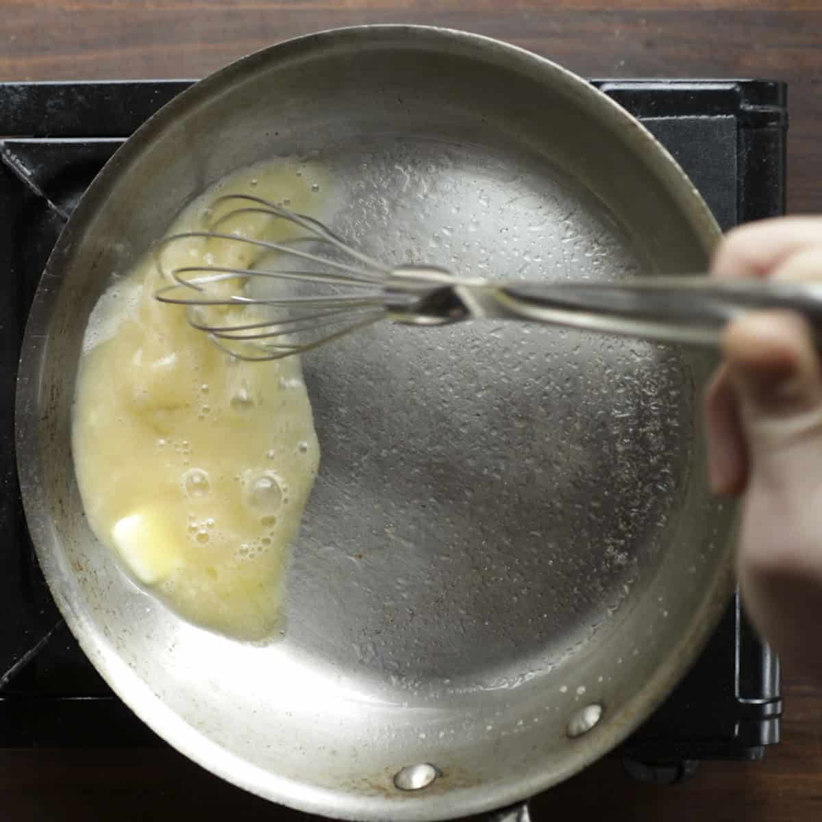 Vigorously whisking a pan of brown butter sauce to melt the butter and make it creamy. 