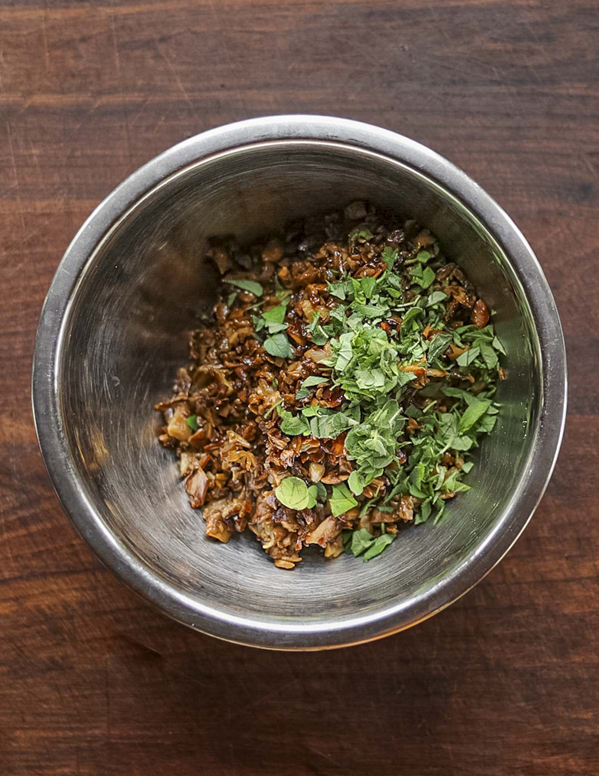 Mixing cooked porcini mushrooms in a bowl with chopped fresh oregano. 