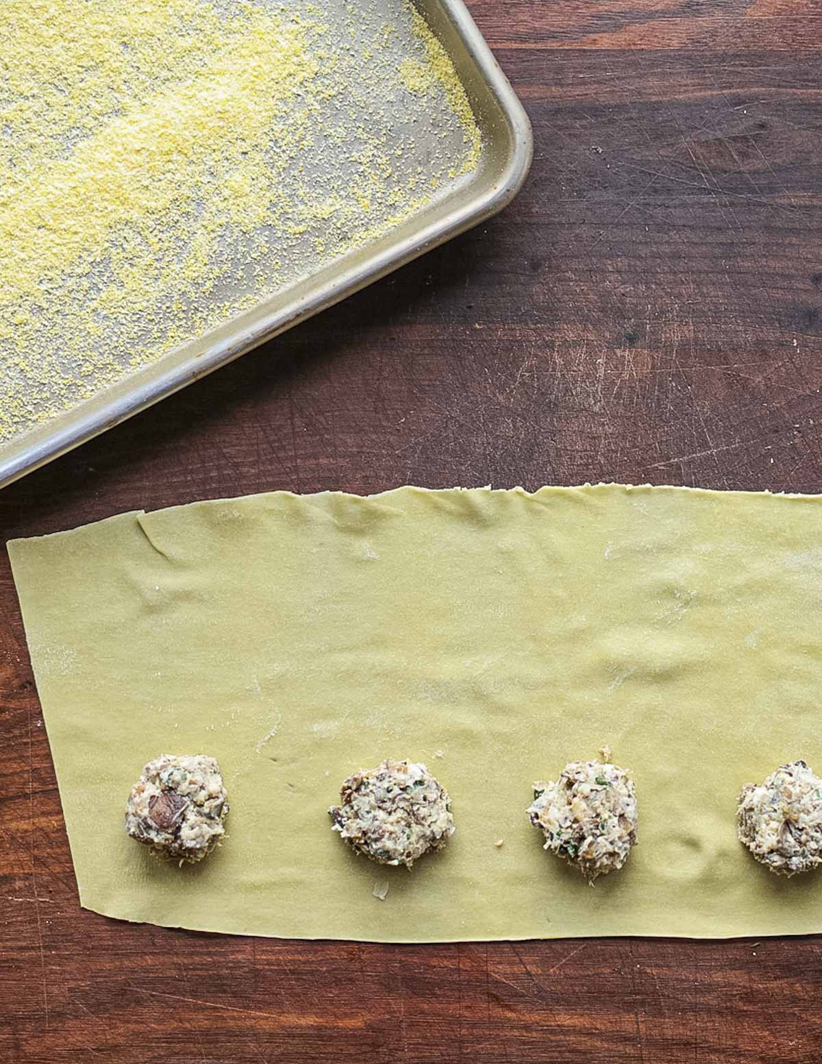 Portioning spoonfuls of porcini mushroom filling on pasta sheets to make ravioli. 