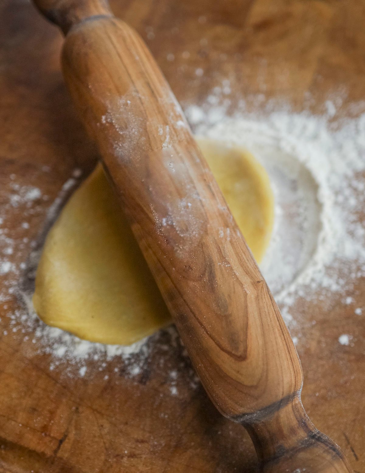 Using a small rolling pin to roll out a piece of pasta dough on a floured cutting board. 