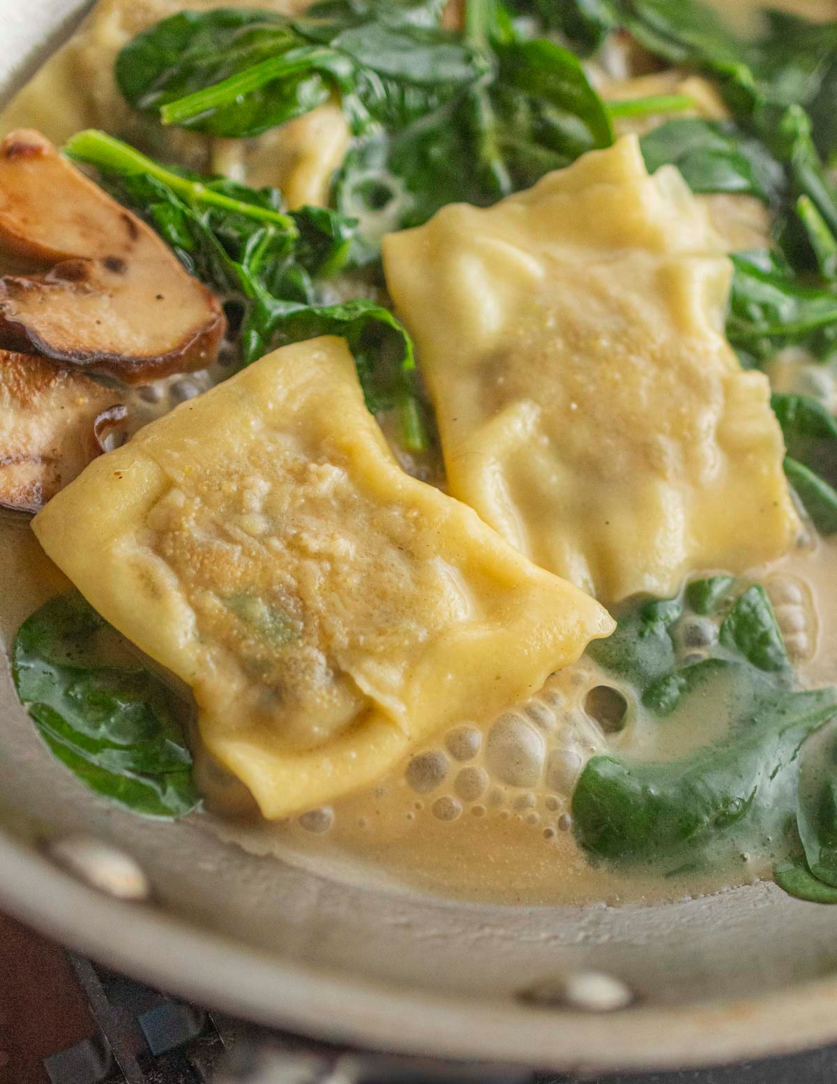 Cooked porcini ravioli simmering in a brown butter sauce with spinach and sauteed porcini. 