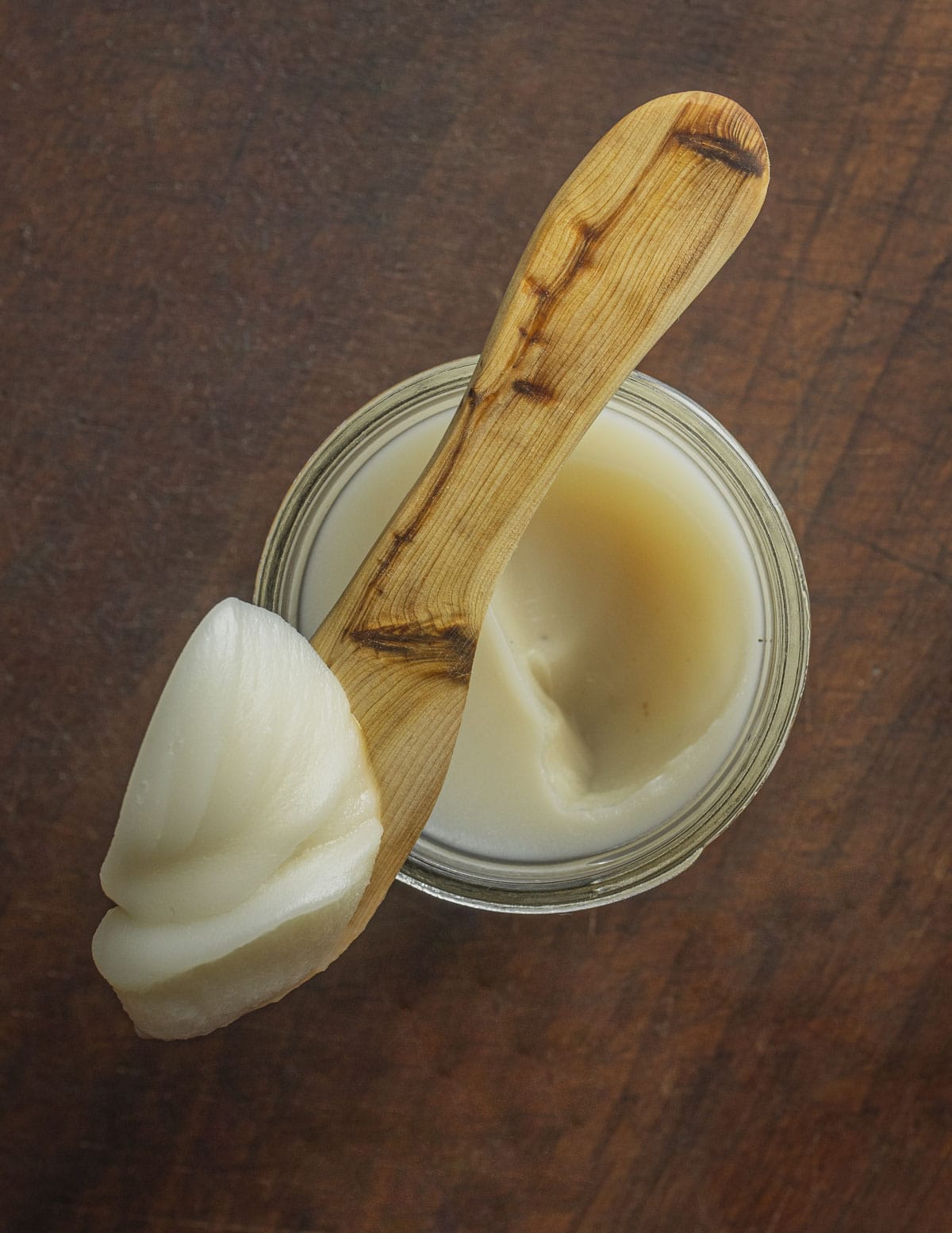 Goose fat spread on a small wooden spatula placed over a jar of goose fat. 