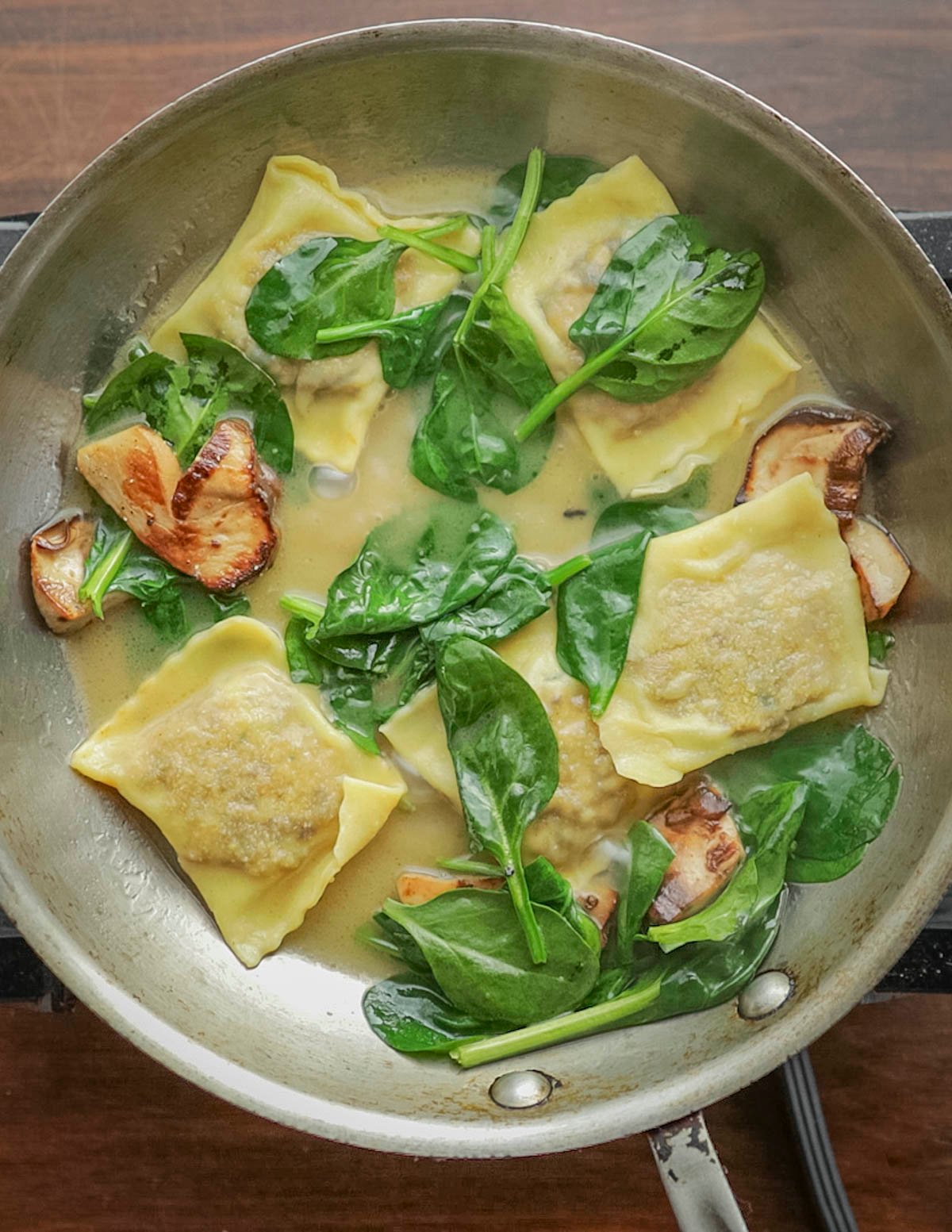 Adding spinach, mushrooms and cooked ravioli to a pan of brown butter sauce. 