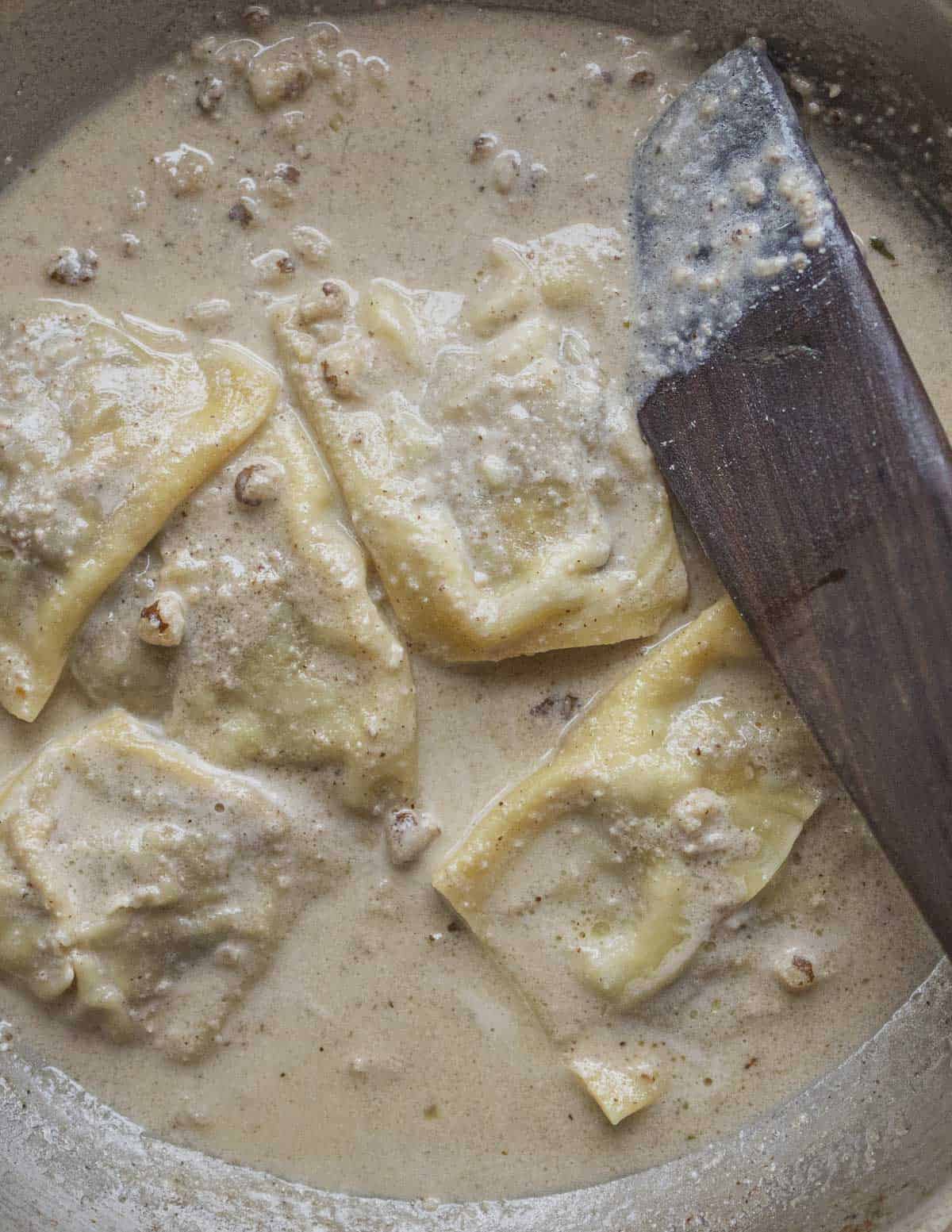 Fresh ravioli simmering in a pan of walnut salsa di noci. 