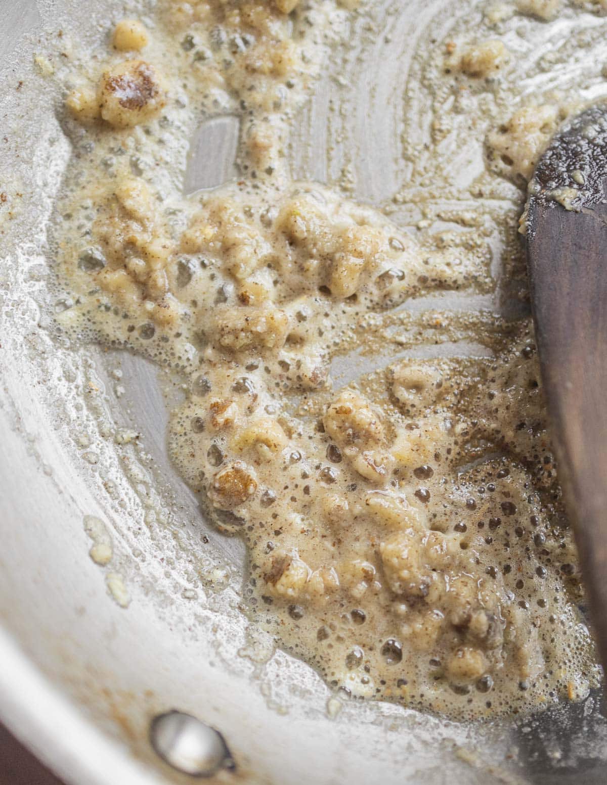 A close up image showing ground black walnuts being cooked in a pan and getting browned. 