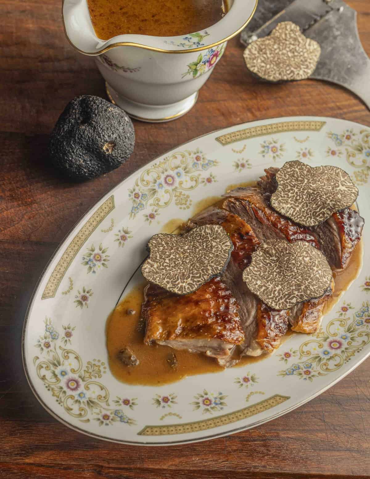 Roast goose sliced on a plate garnished with black truffle sauce. 