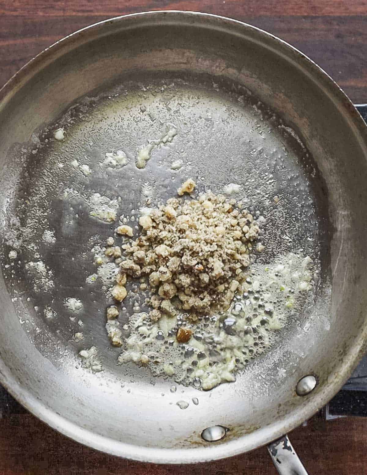 Adding ground walnuts to a pan of garlic and butter. 