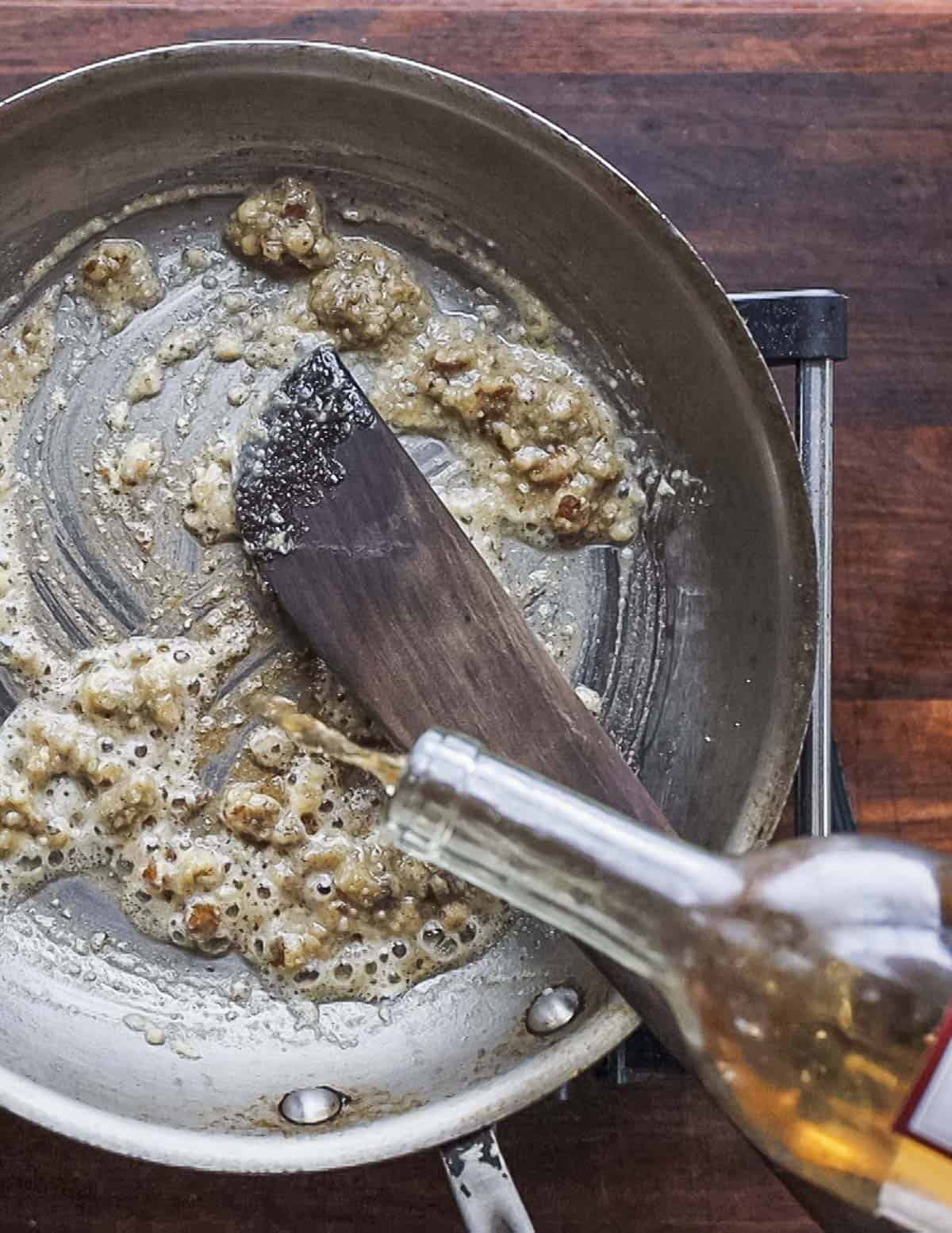 Adding dry white wine to a pan of salsa di noci walnut sauce. 