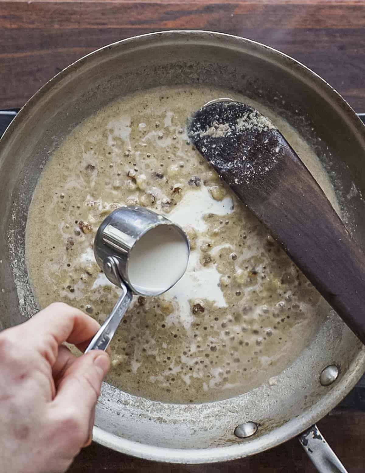 Adding heavy cream to a pan of walnut sauce. 